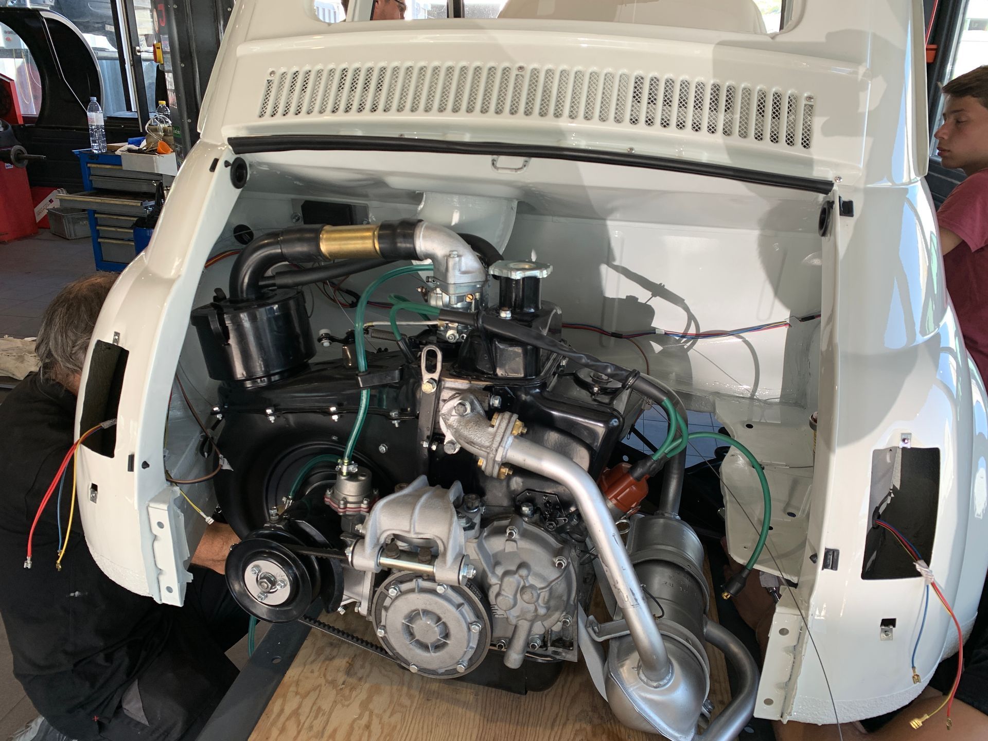 Un homme travaille sur le moteur d’une voiture blanche.