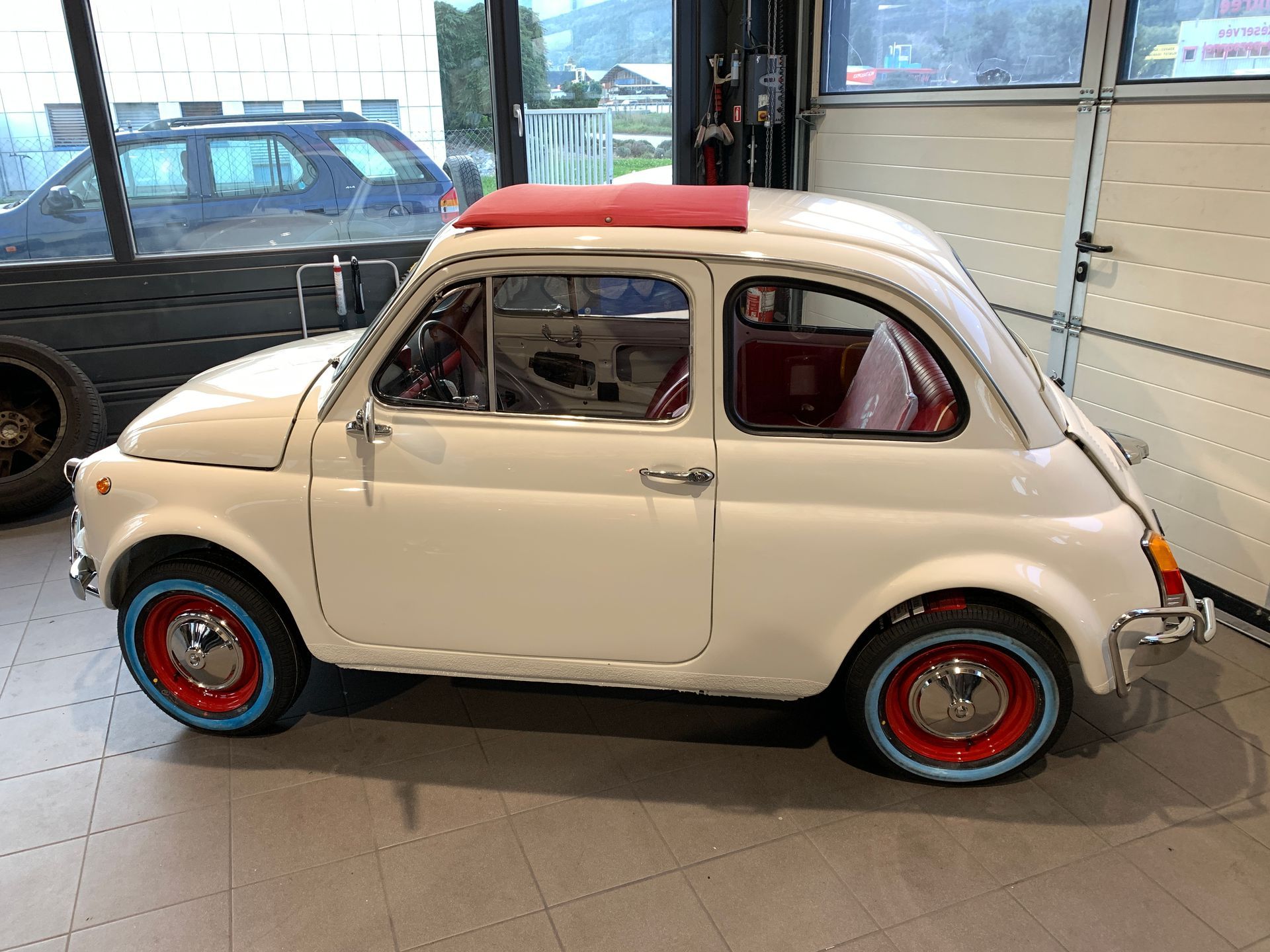 Une voiture blanche aux roues rouges et bleues est garée dans un garage.