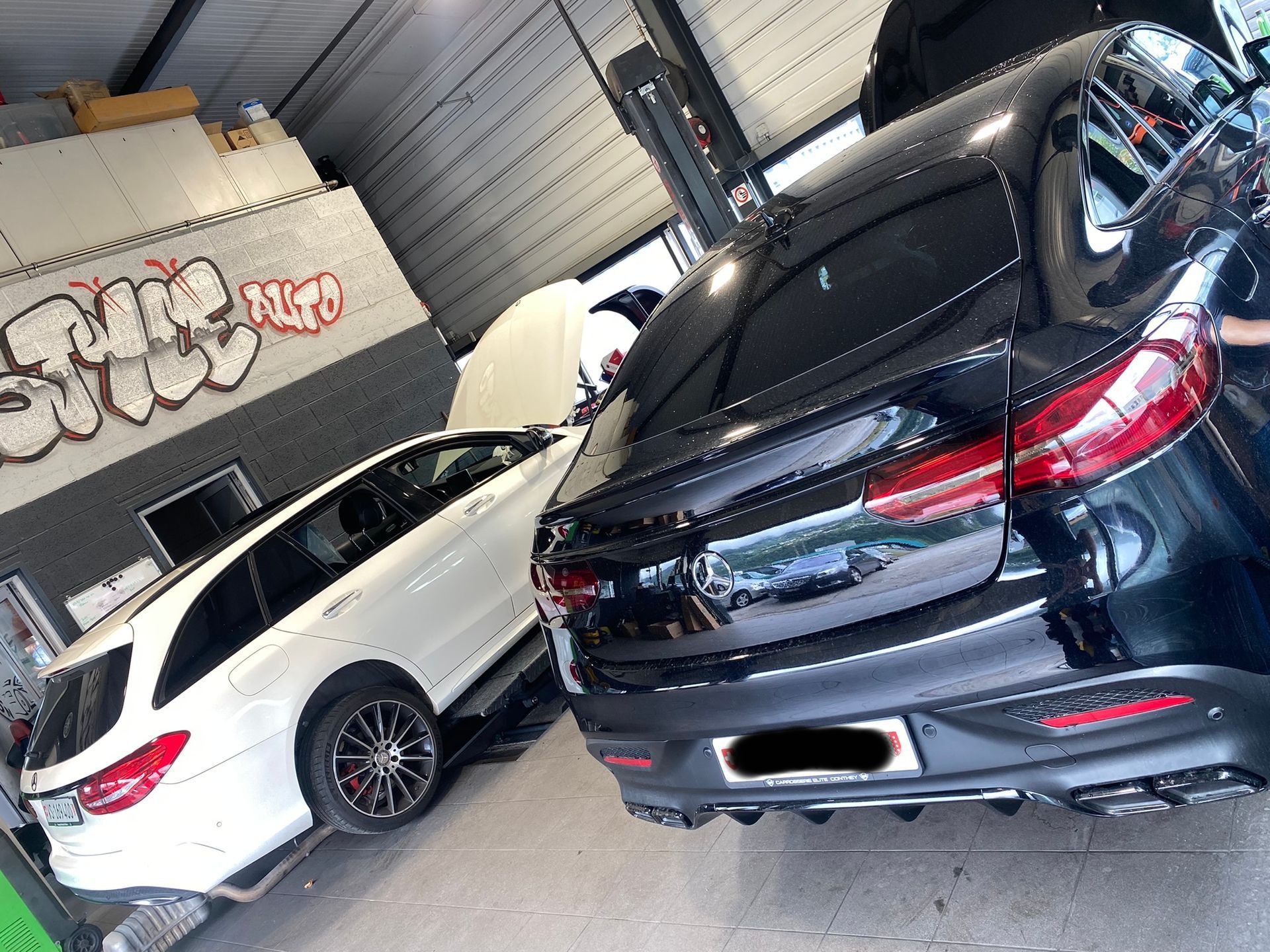 Une voiture noire est garée à côté d’une voiture blanche dans un garage.