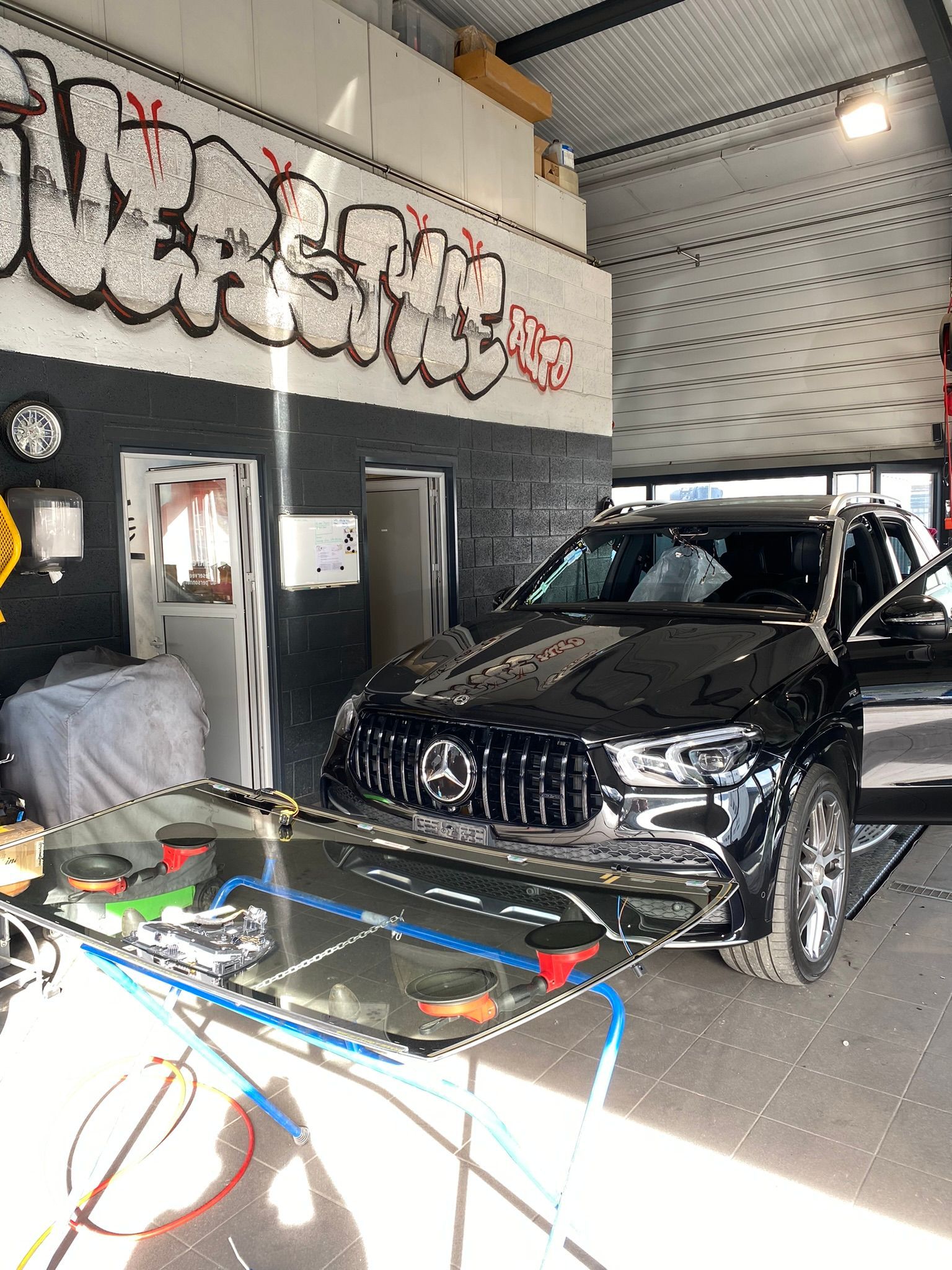 Une voiture noire est garée dans un garage avec des graffitis sur le mur.