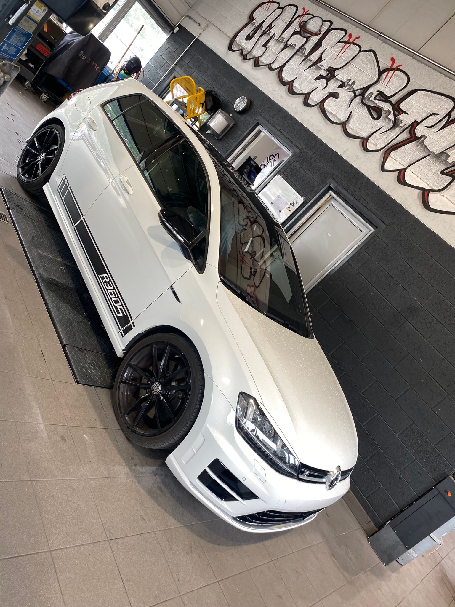 Une voiture blanche est garée devant un mur avec des graffitis dessus.