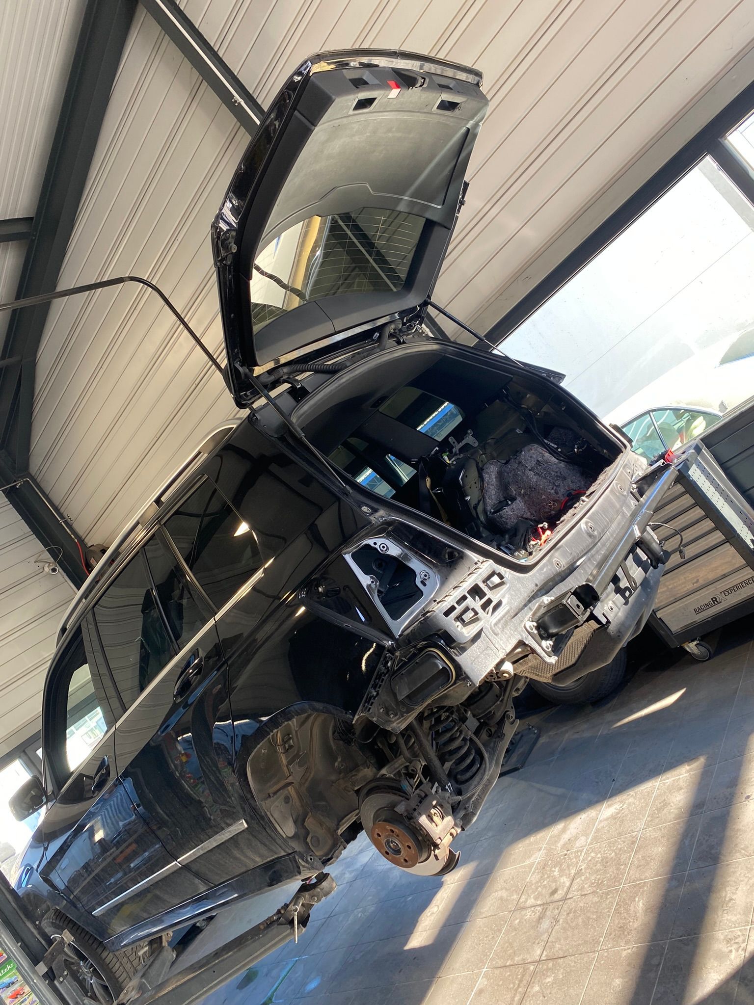 Une voiture est démontée dans un garage avec le coffre ouvert.