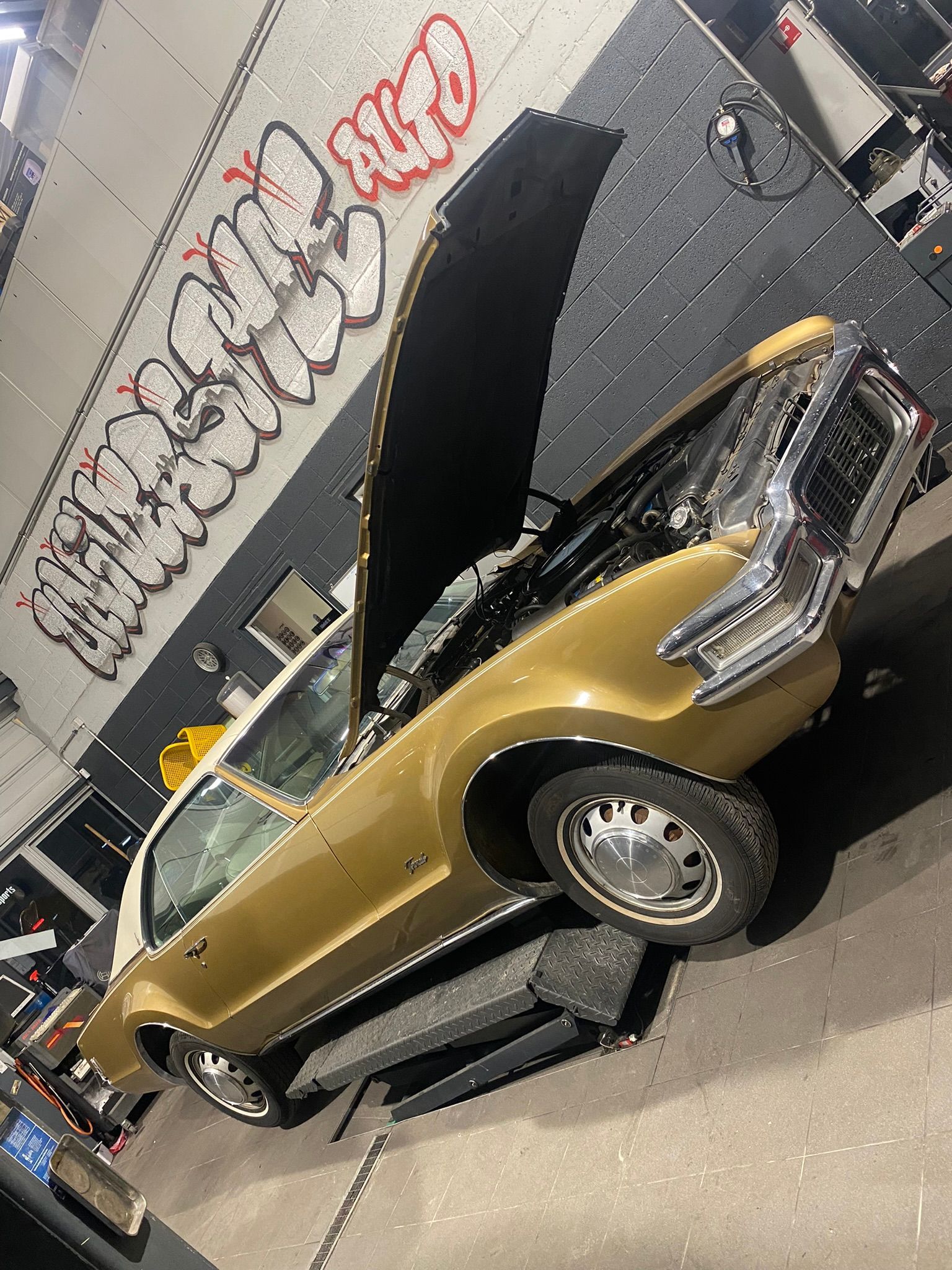 Une voiture dorée avec le capot relevé est garée dans un garage.