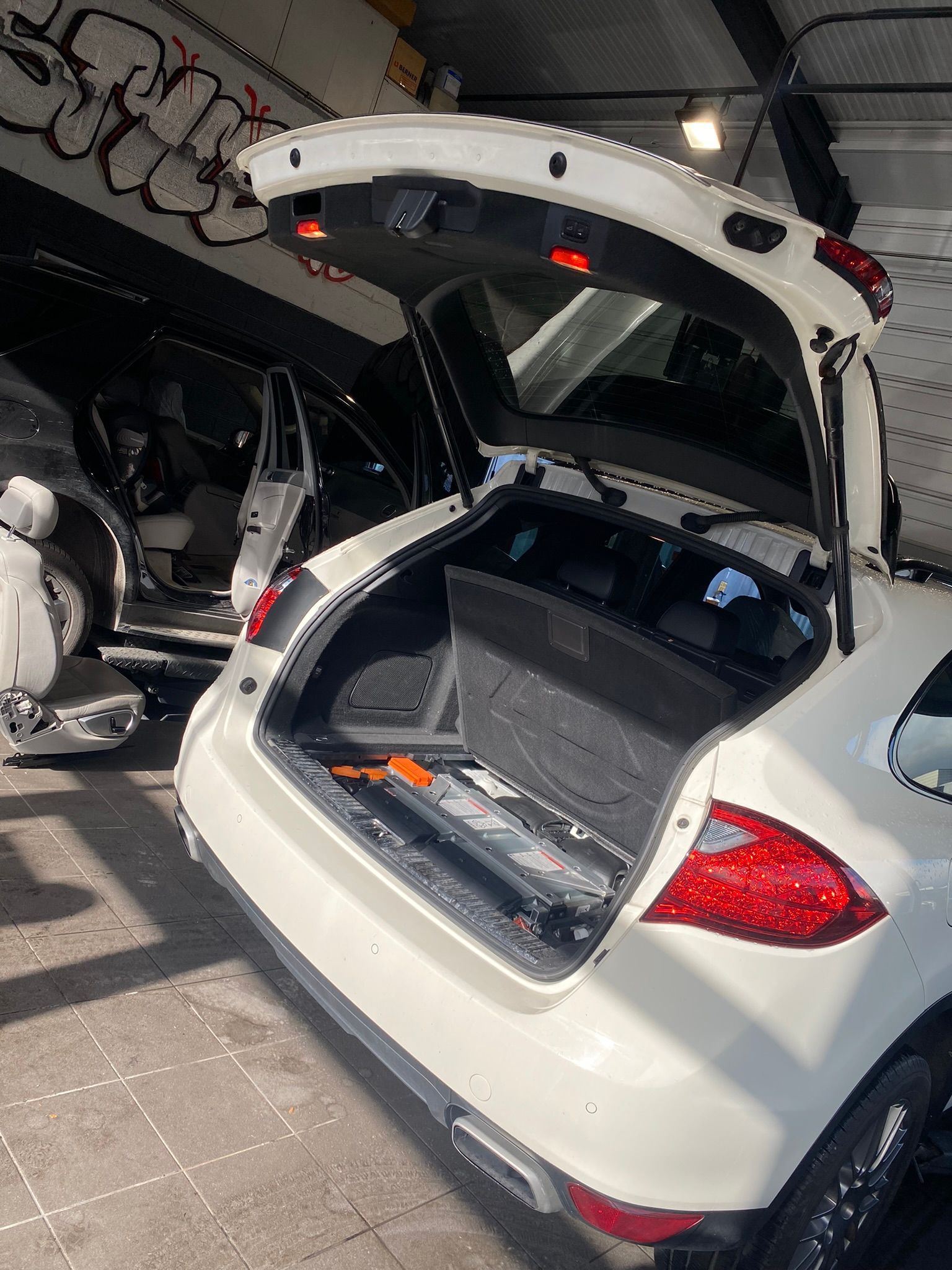 Une voiture blanche avec le coffre ouvert est garée dans un garage.