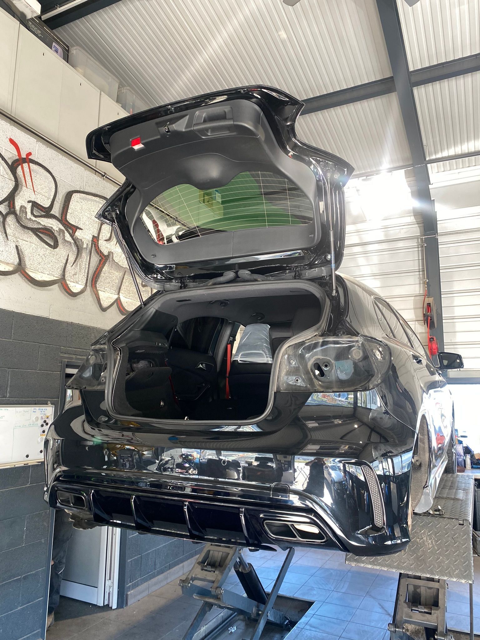 Une voiture noire avec le coffre ouvert est assise sur un ascenseur dans un garage.