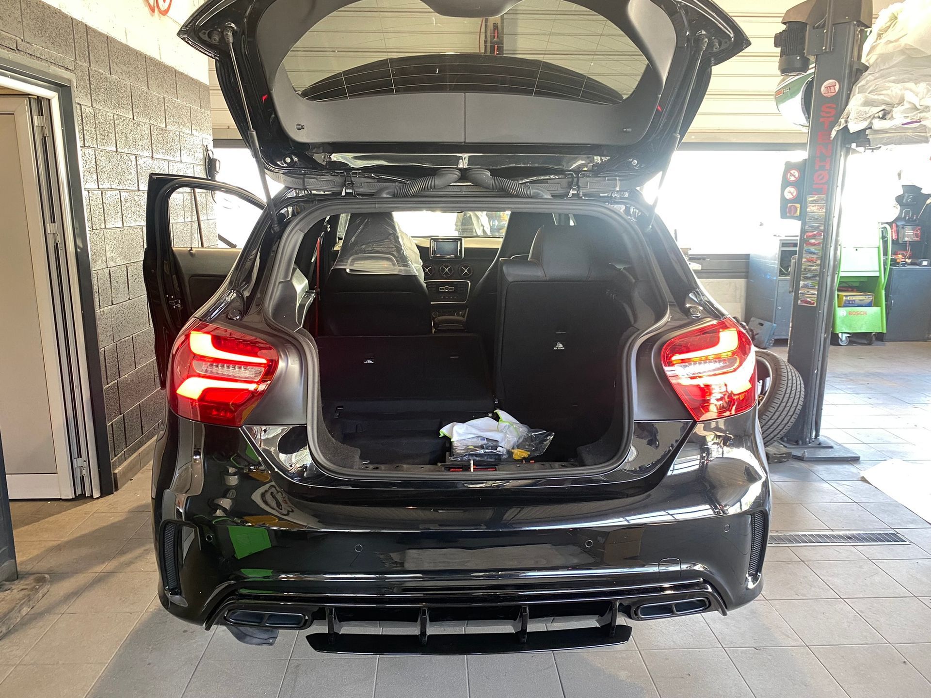Une voiture noire avec le coffre ouvert dans un garage.