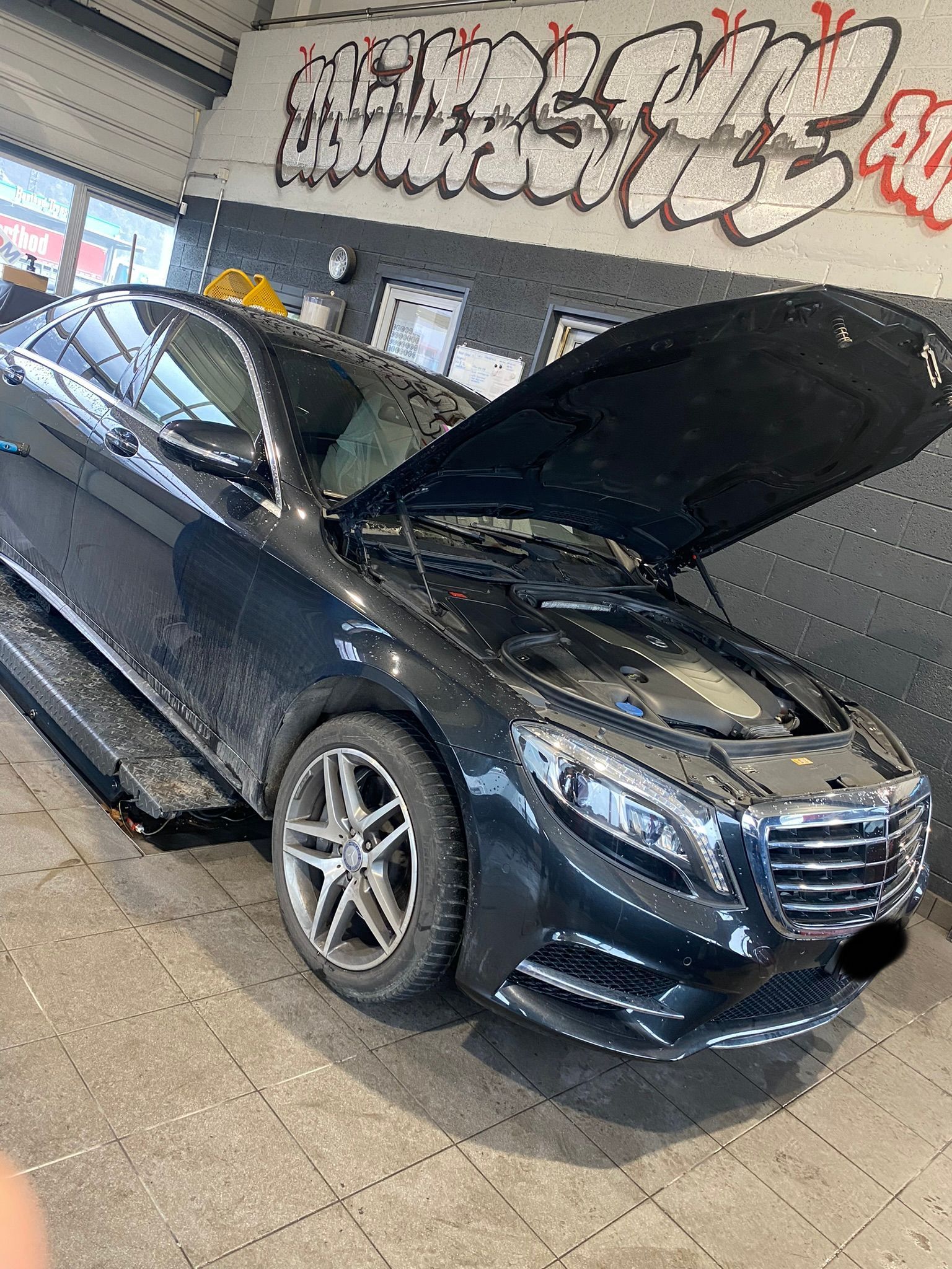 Une Mercedes Benz noire avec le capot ouvert est garée dans un garage.