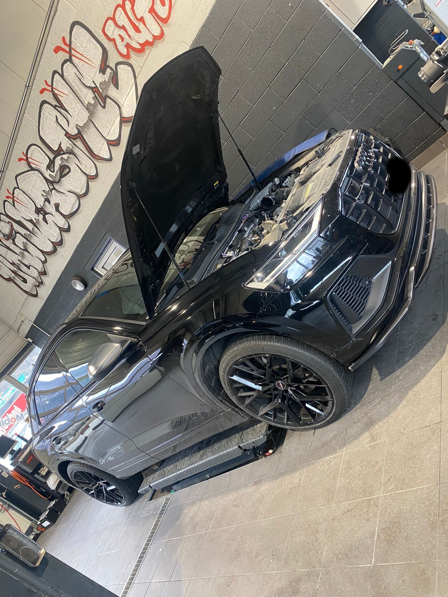 Une voiture noire avec le capot relevé est garée dans un garage.