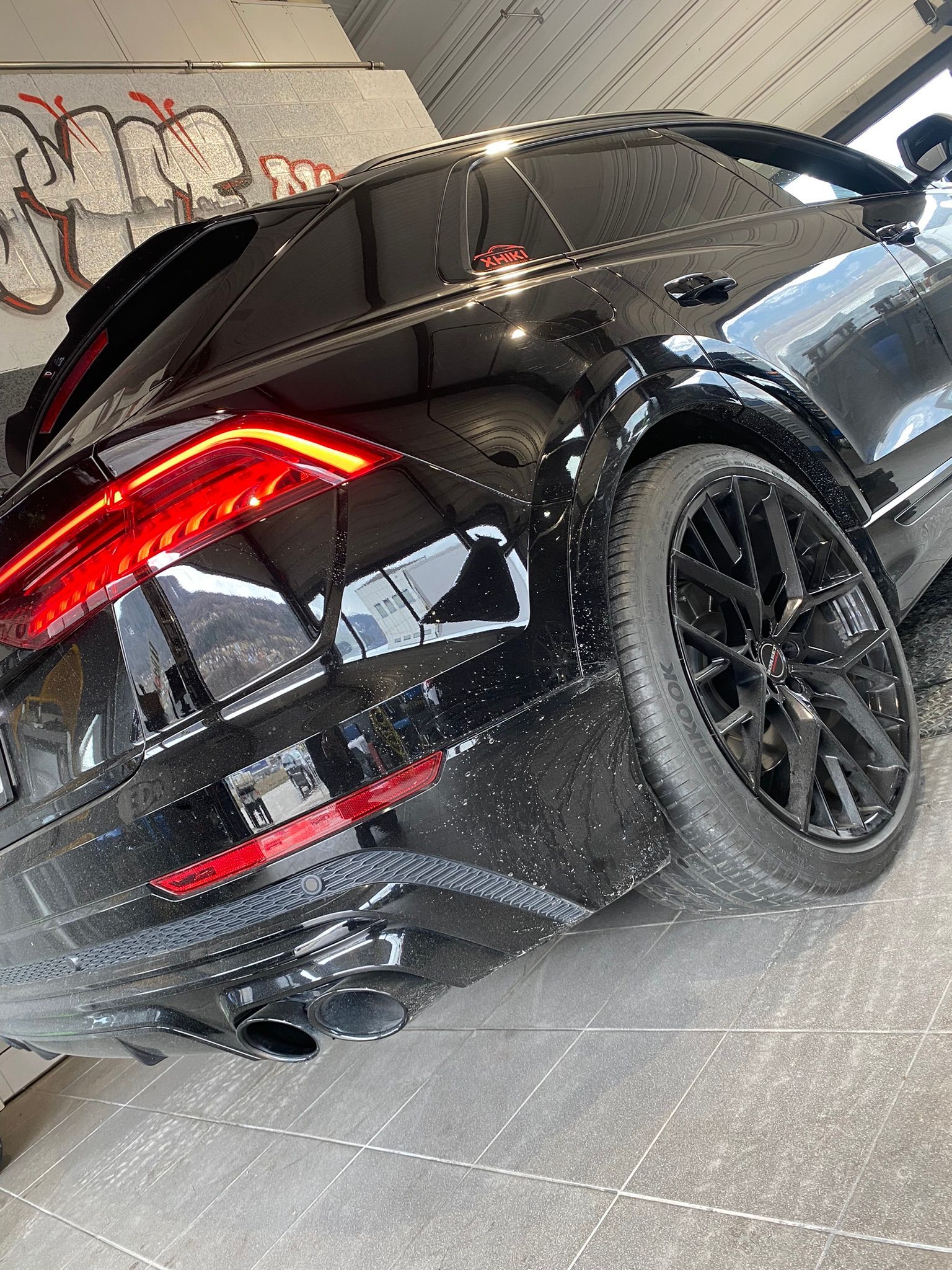 Une voiture noire est garée dans un garage avec des graffitis sur le mur.