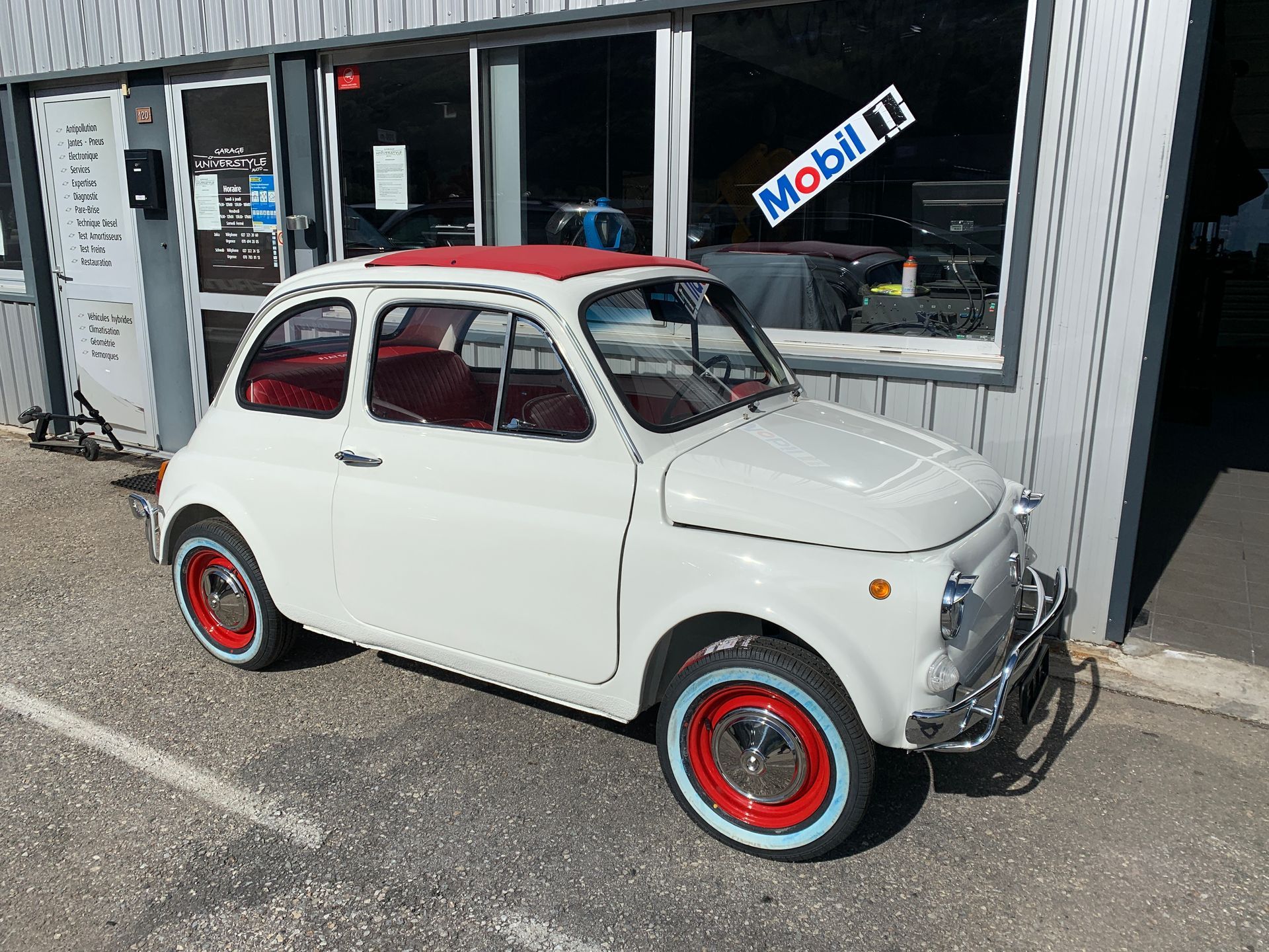 Une voiture blanche aux roues rouges est garée devant un immeuble.