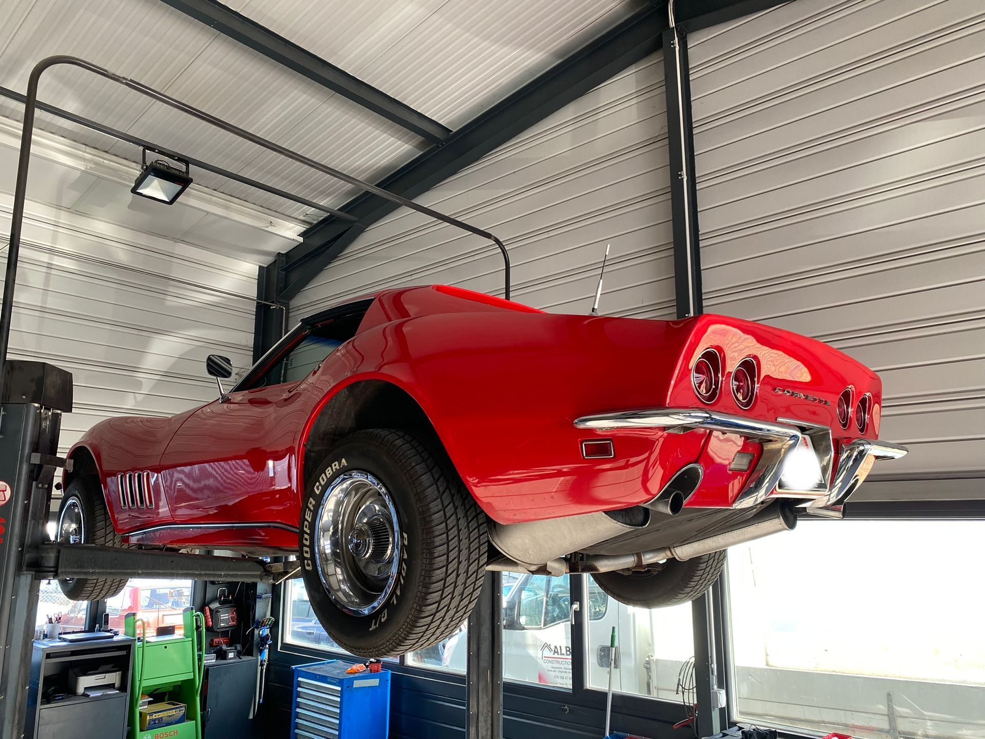 Une corvette rouge est assise sur un ascenseur dans un garage.