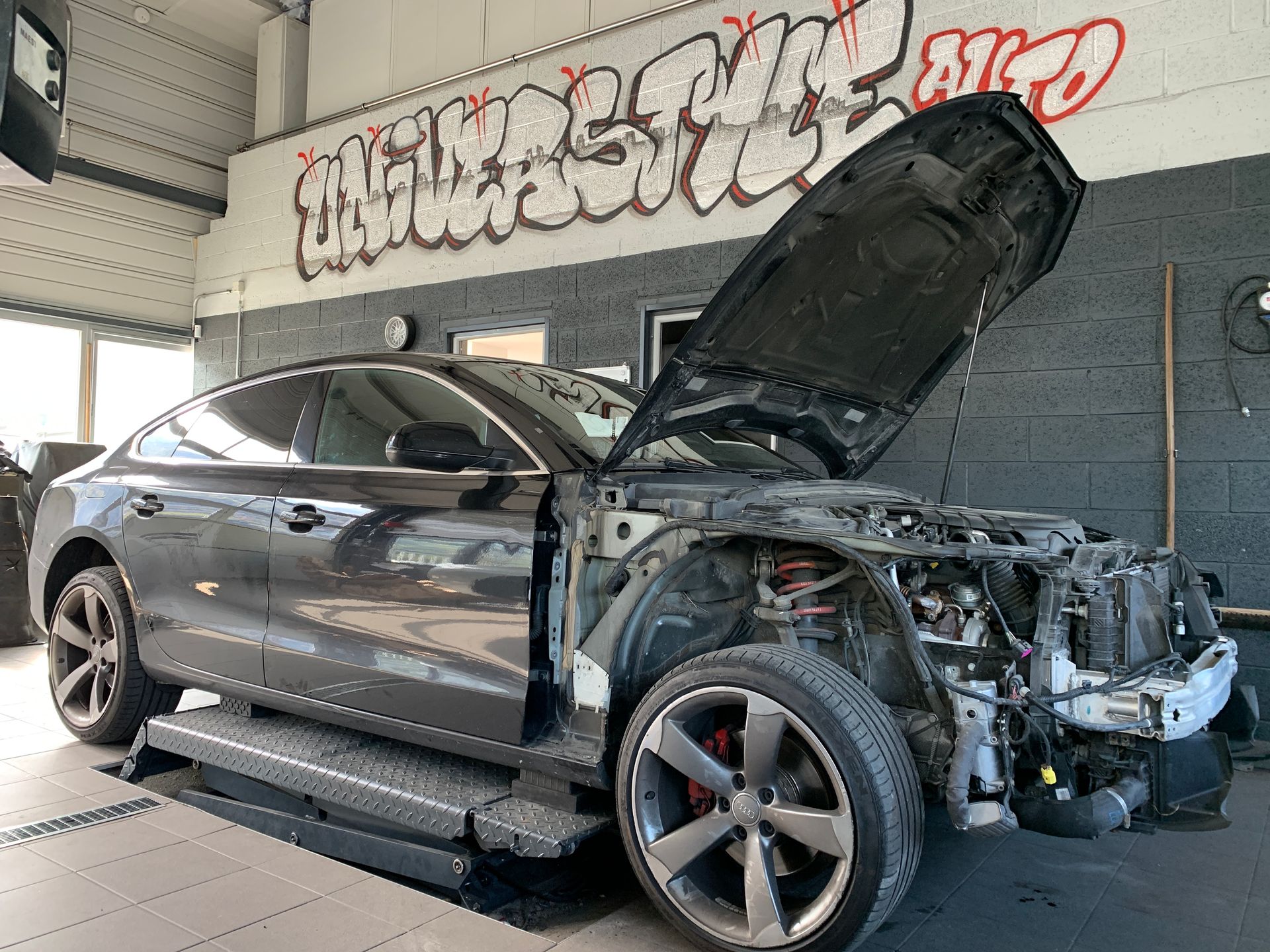 Une voiture avec le capot relevé est posée sur un ascenseur dans un garage.