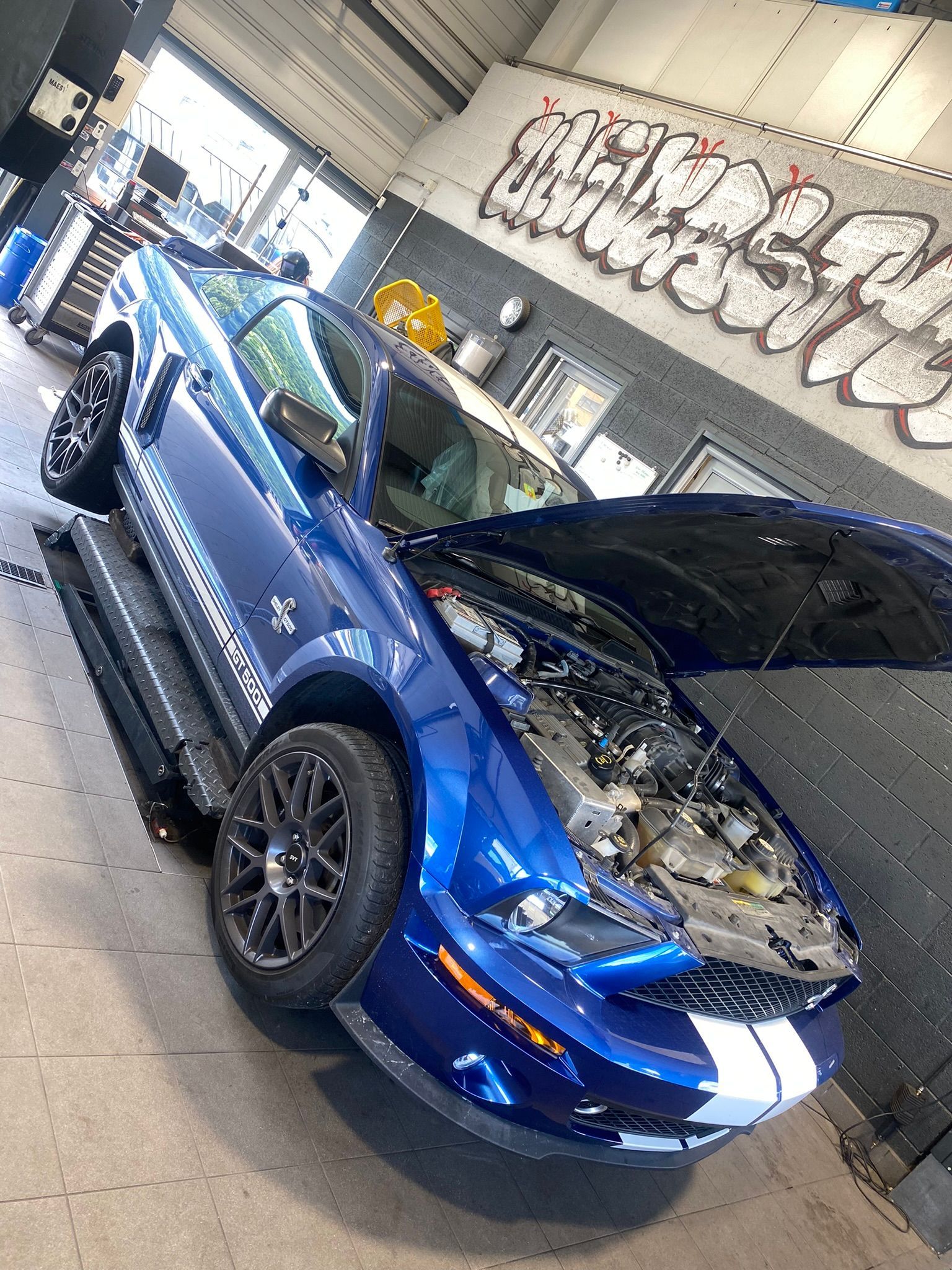Une Mustang bleue est garée dans un garage avec son capot ouvert.