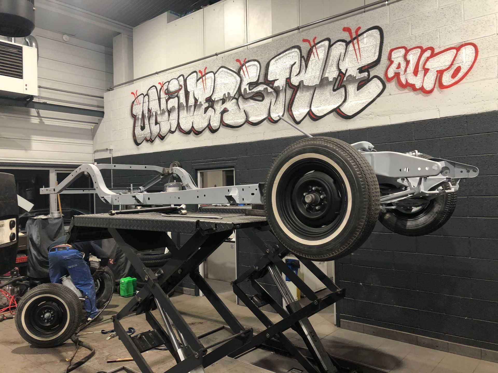 Une voiture est posée sur un ascenseur dans un garage avec des graffitis sur le mur.