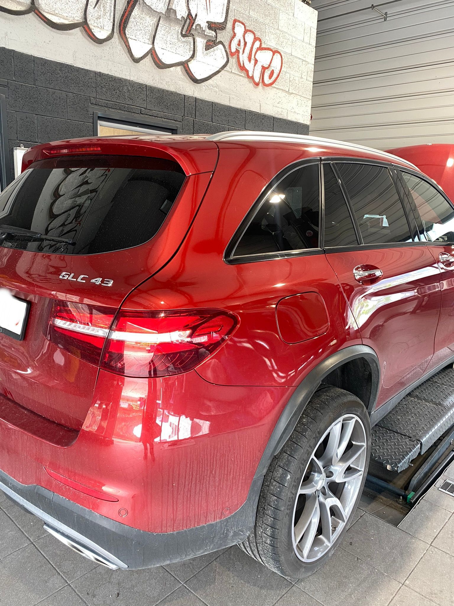 Une voiture rouge est garée devant un immeuble avec des graffitis sur les murs.