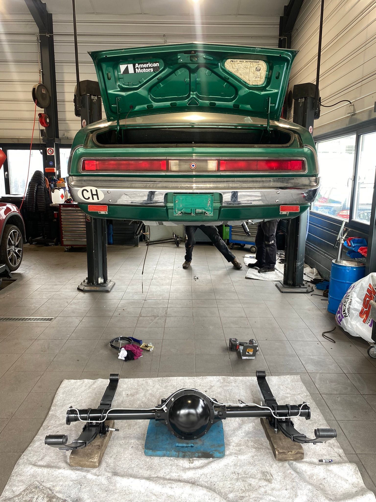 Une voiture verte est assise sur un ascenseur dans un garage avec le coffre ouvert.