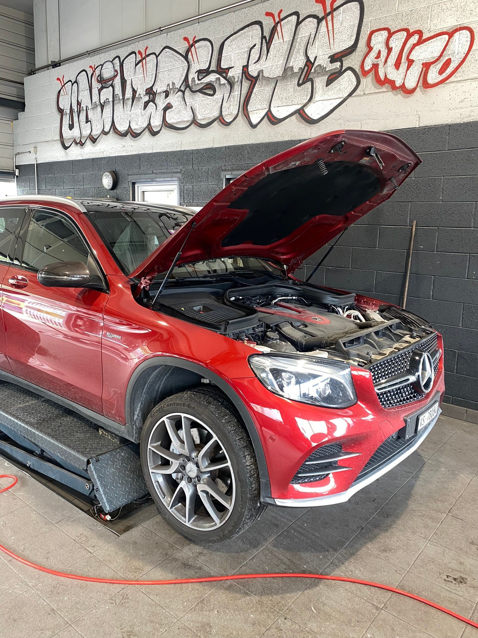 Une Mercedes Benz GLC rouge est garée dans un garage avec son capot ouvert.