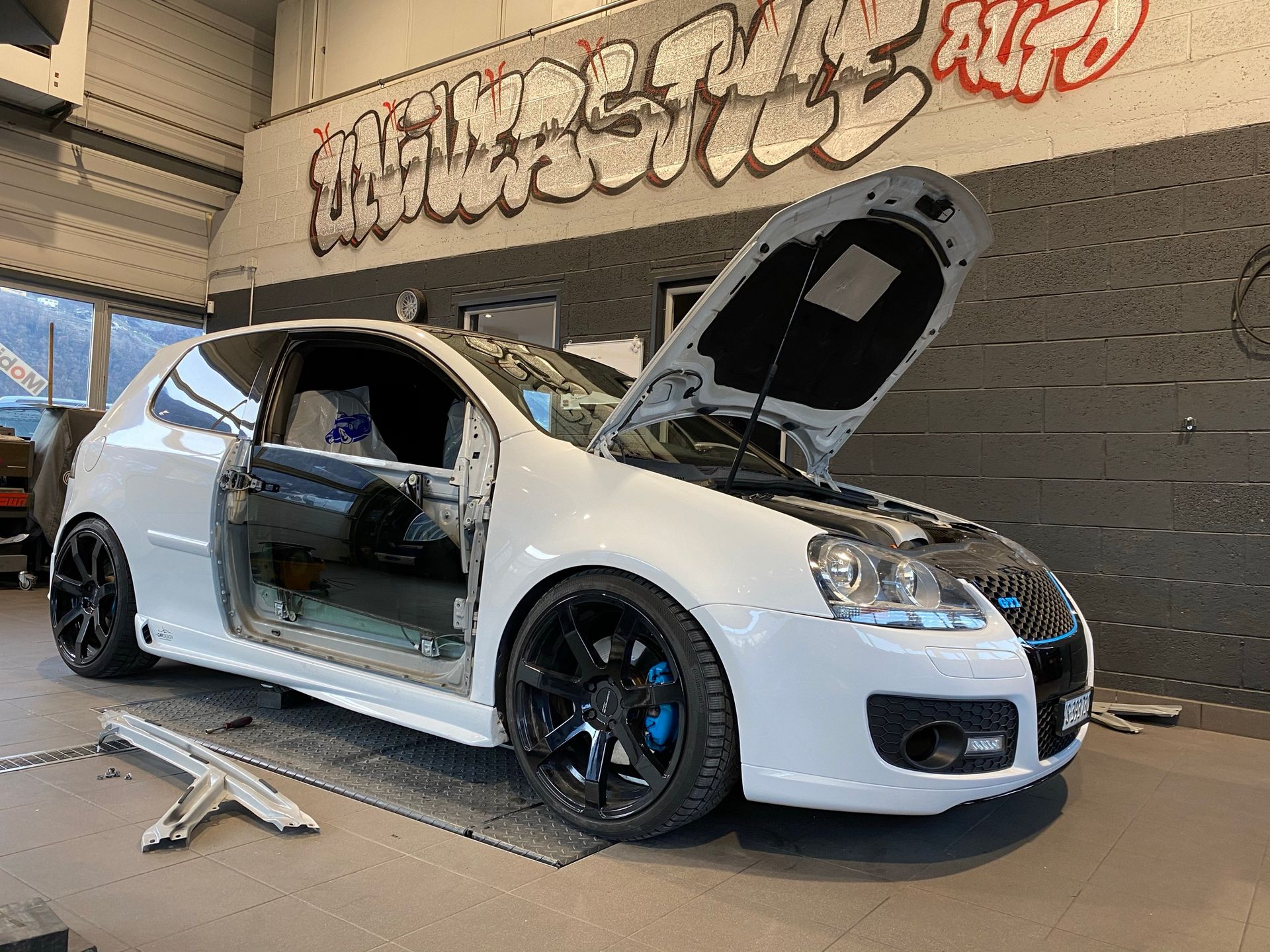 Une voiture blanche avec le capot relevé est assise dans un garage.