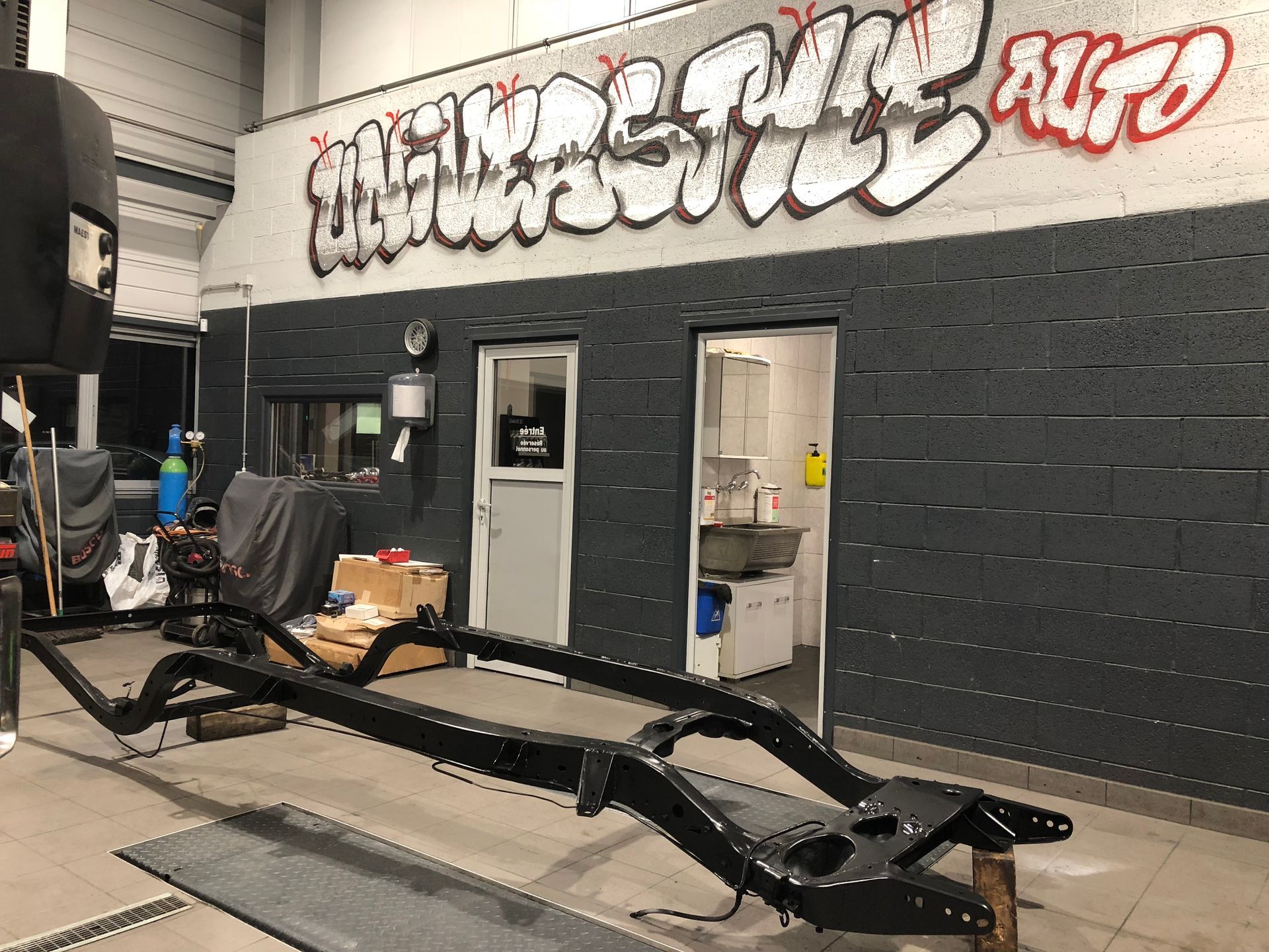 Un châssis de voiture se trouve dans un garage avec des graffitis sur le mur.