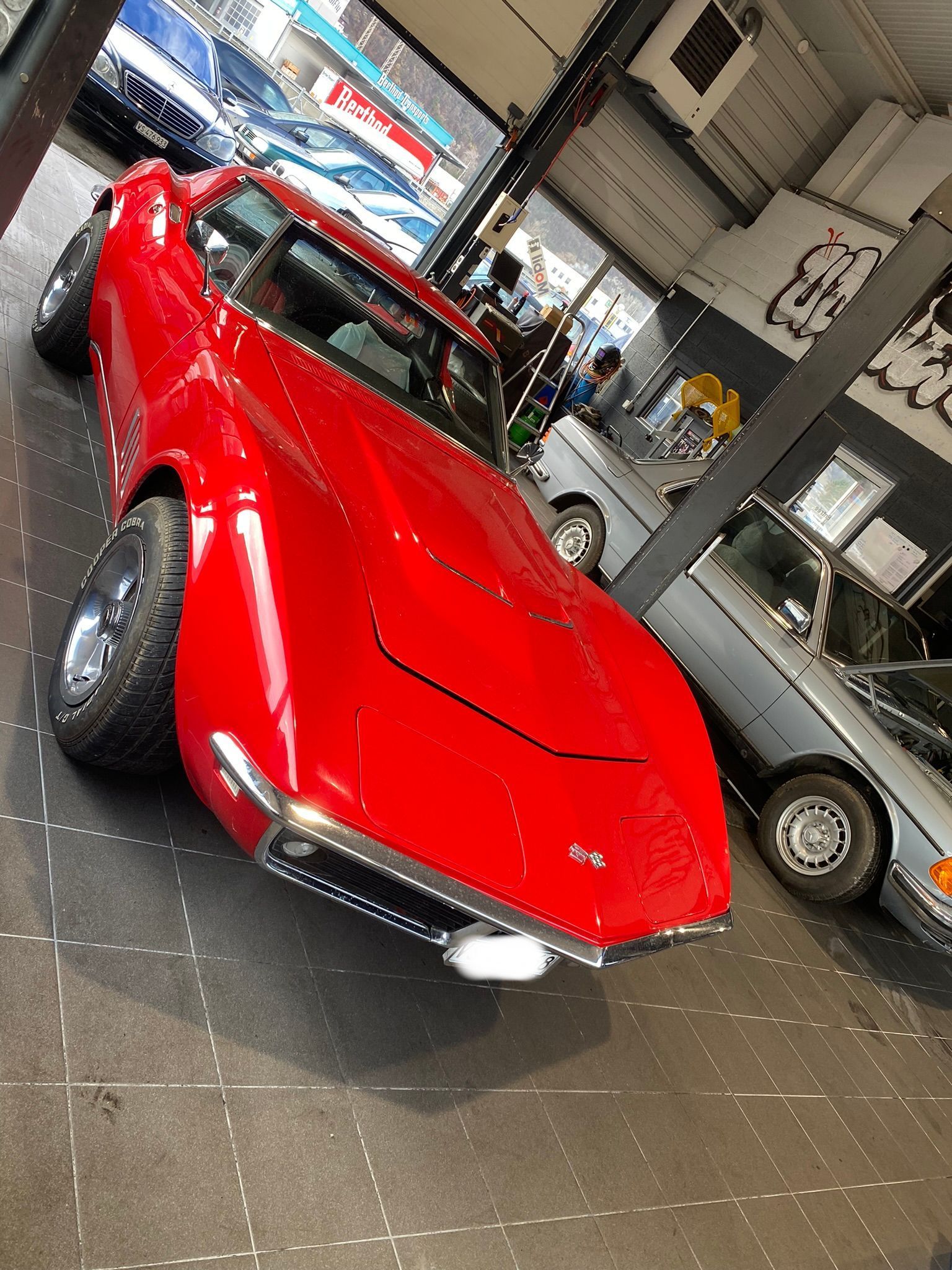 Une corvette rouge est garée dans un garage à côté d'autres voitures.