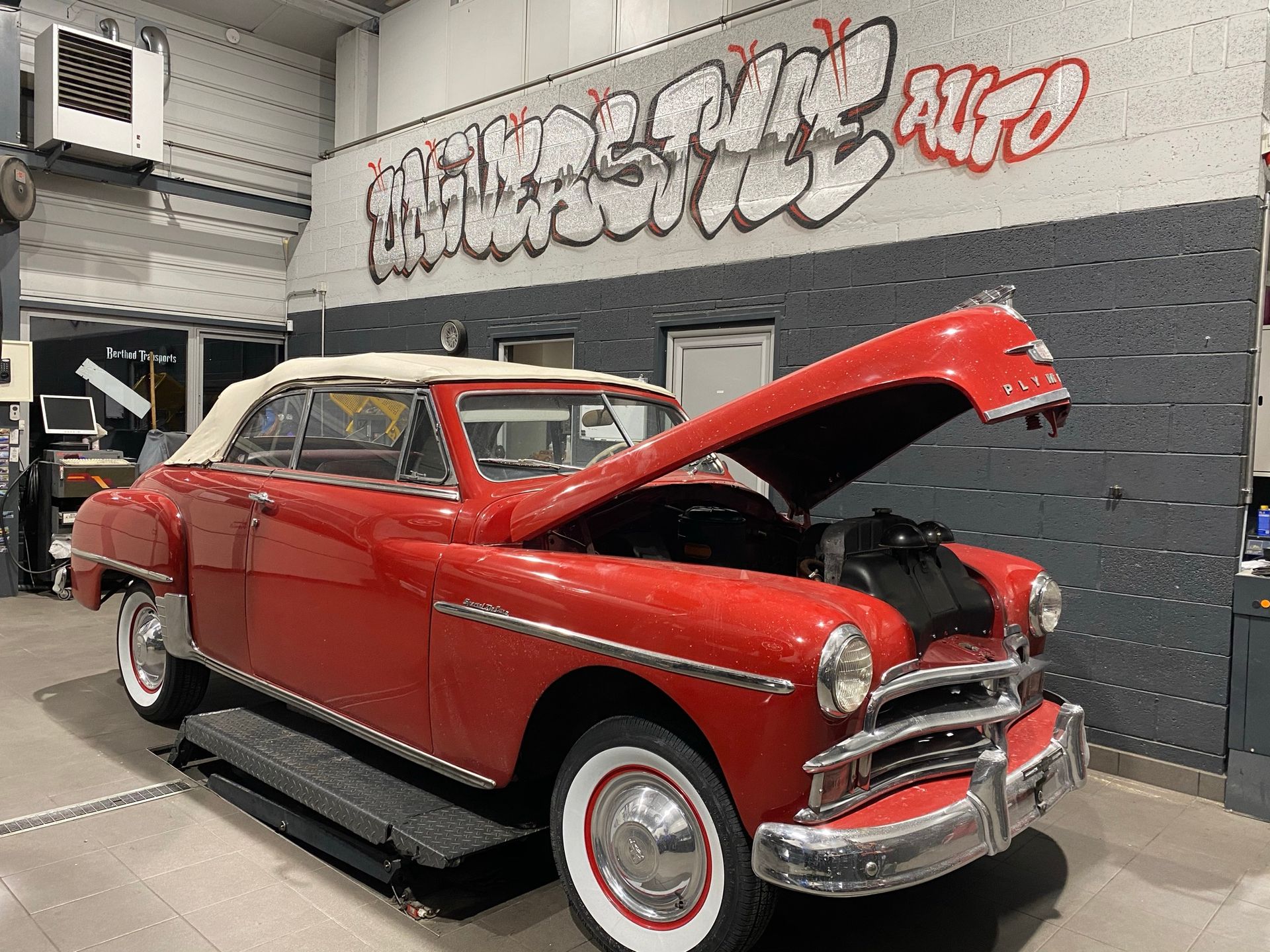 Une voiture rouge avec le capot relevé est garée dans un garage.