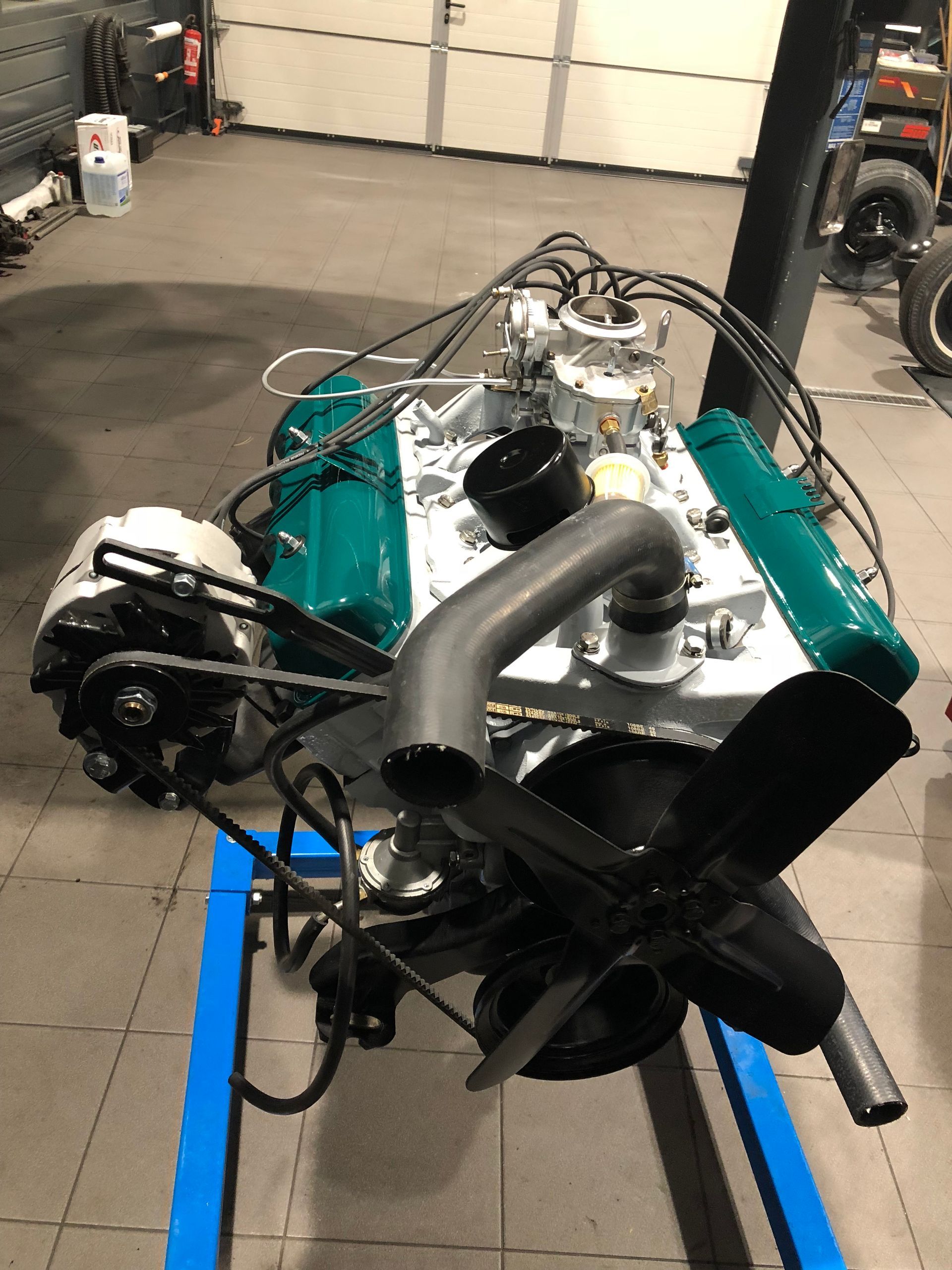 Un moteur de voiture est posé sur un support bleu dans un garage.