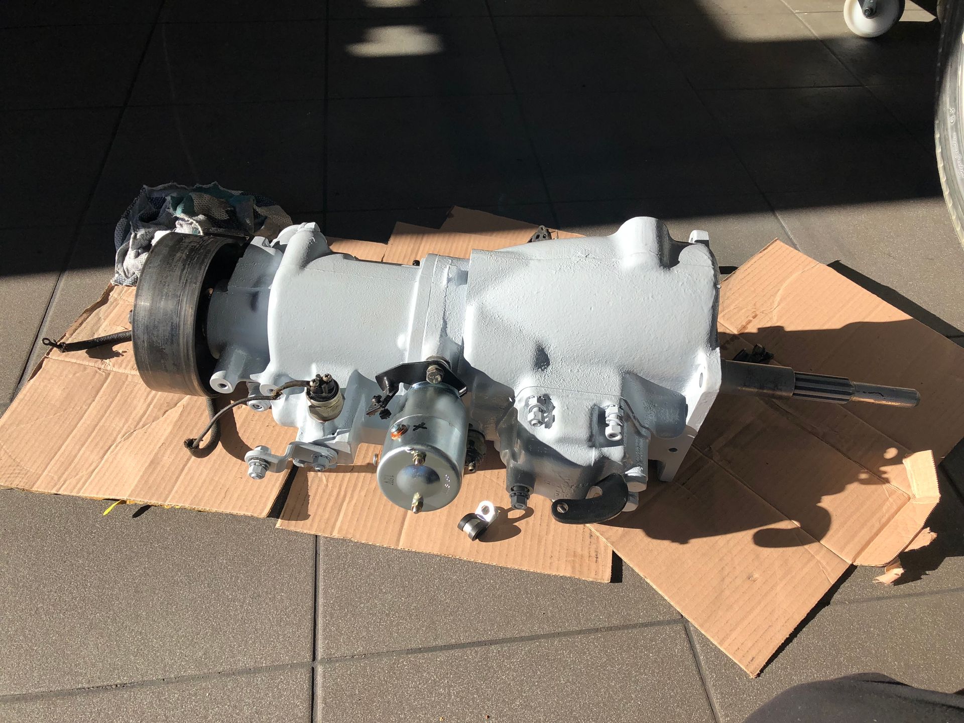 Une boîte de vitesses repose sur un morceau de carton au sol.