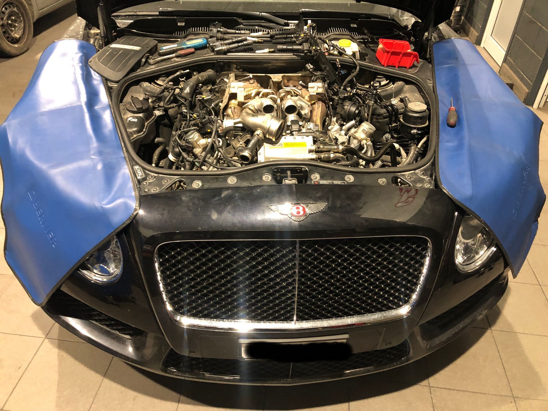 Une voiture noire avec le capot relevé est en cours de réparation dans un garage.