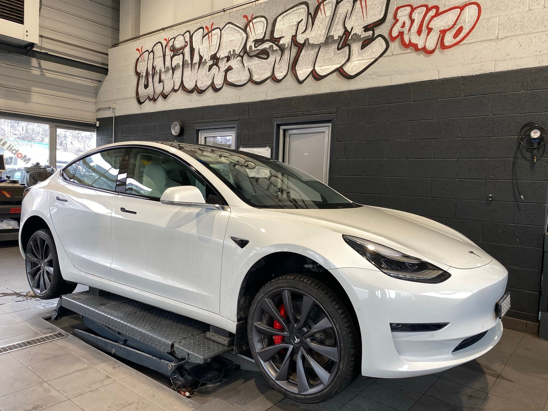 Une Tesla Model 3 blanche est posée sur un ascenseur dans un garage.
