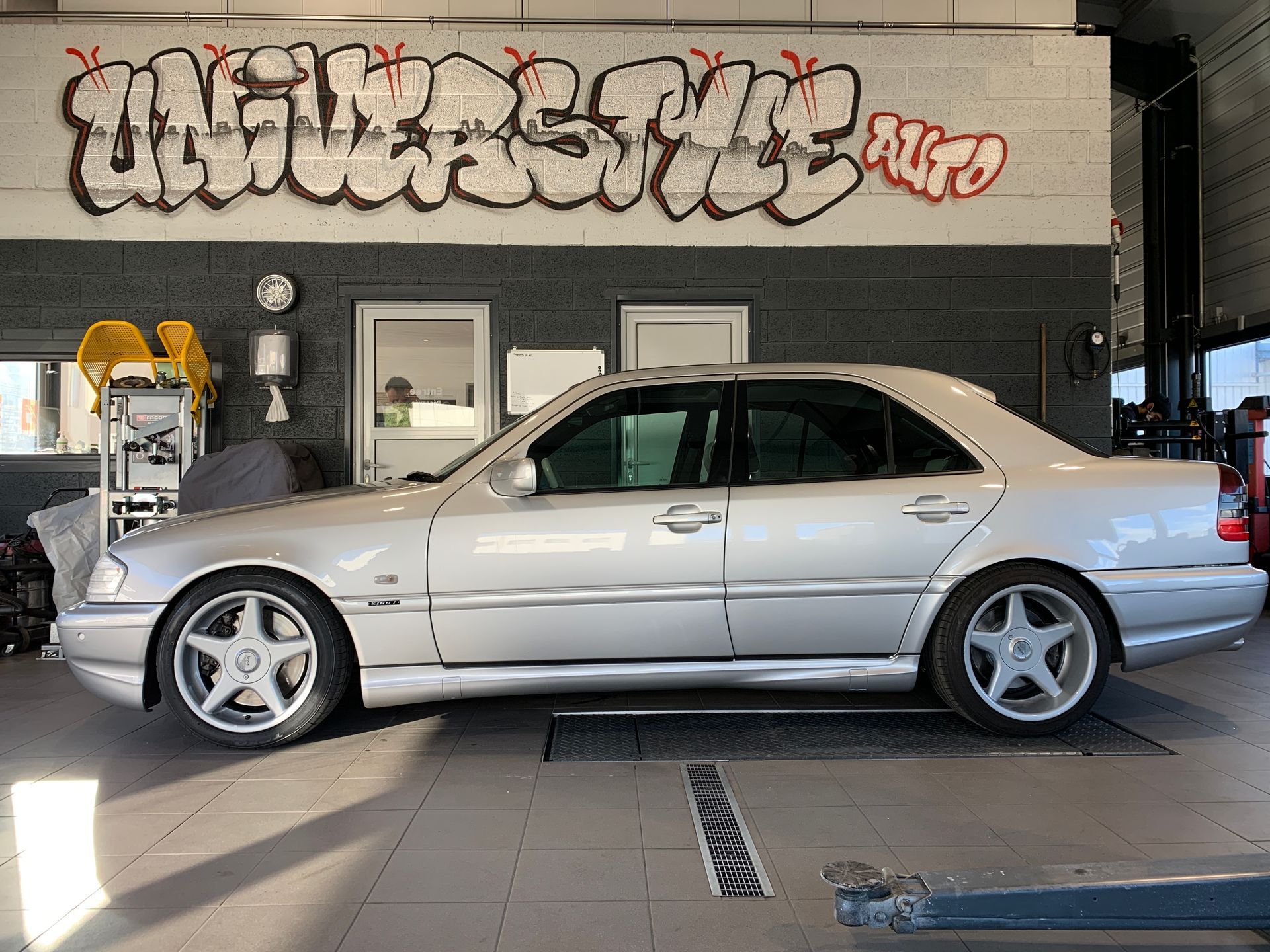 Une voiture argentée est garée dans un garage avec des graffitis sur le mur.