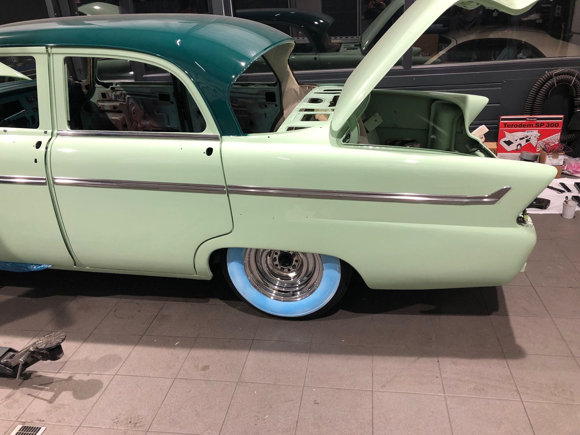 Une voiture verte avec le capot ouvert est garée dans un garage.