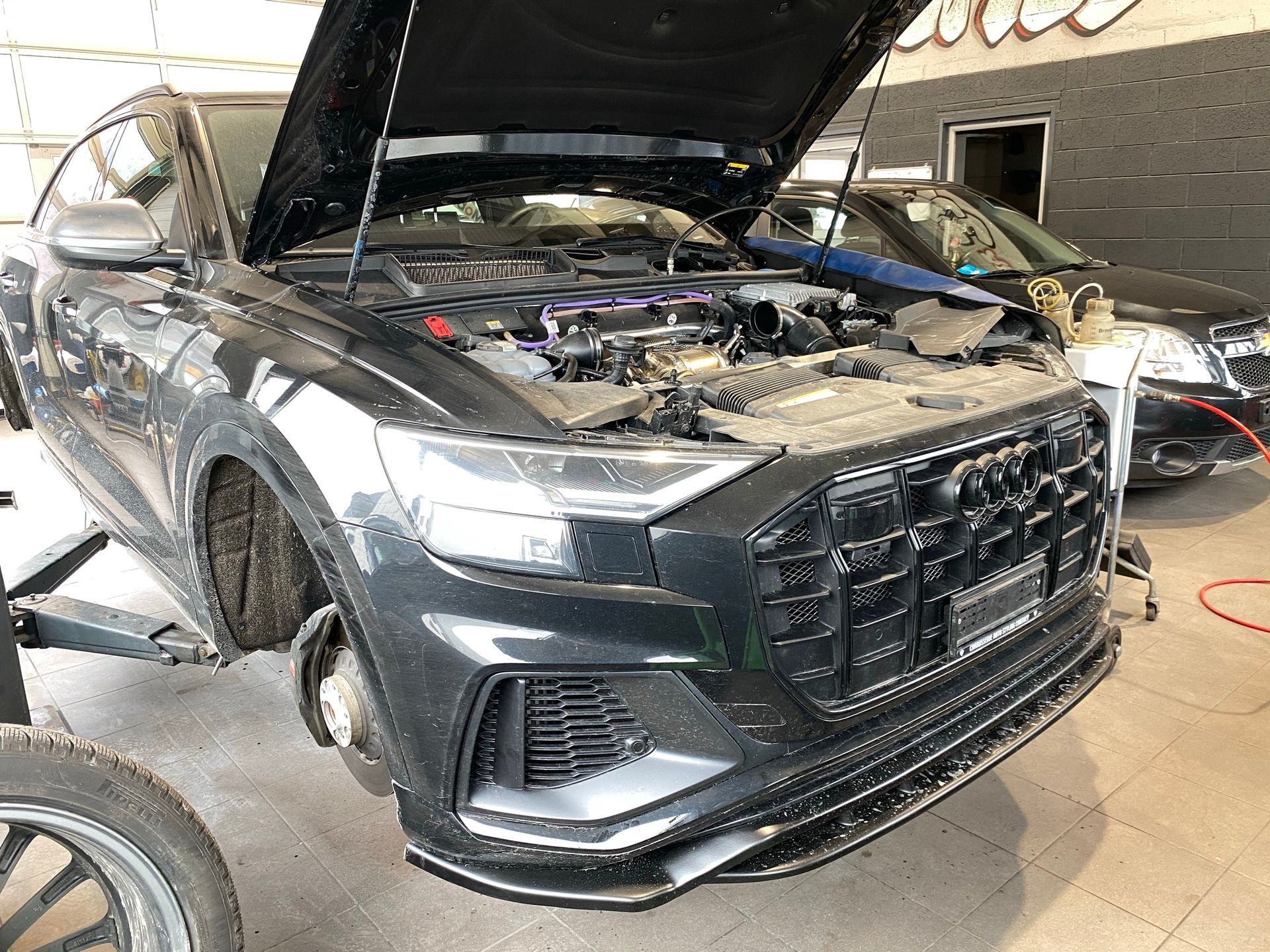 Une voiture noire avec le capot relevé est en cours de réparation dans un garage.
