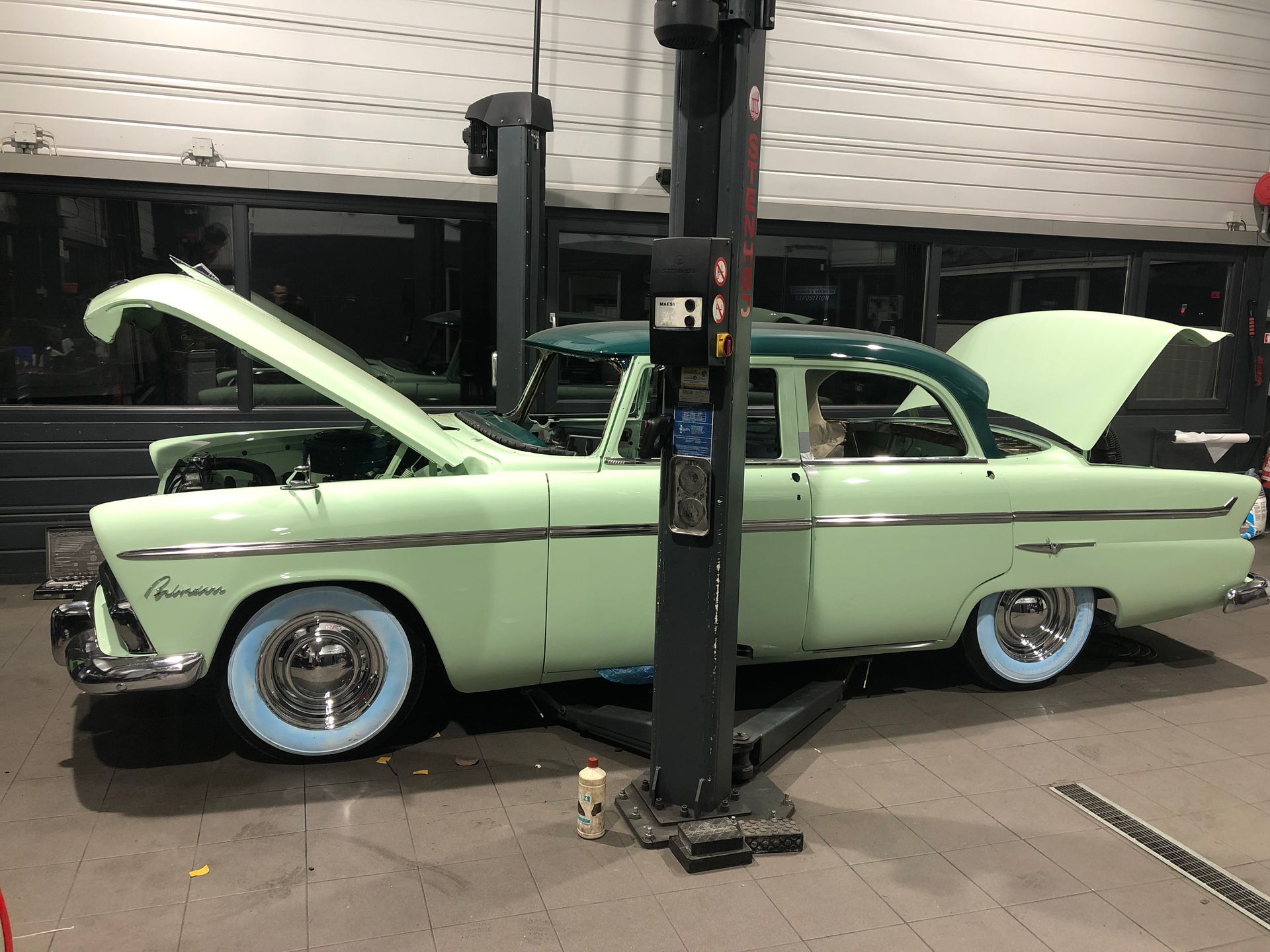 Une voiture verte avec le capot relevé est sur un ascenseur dans un garage.