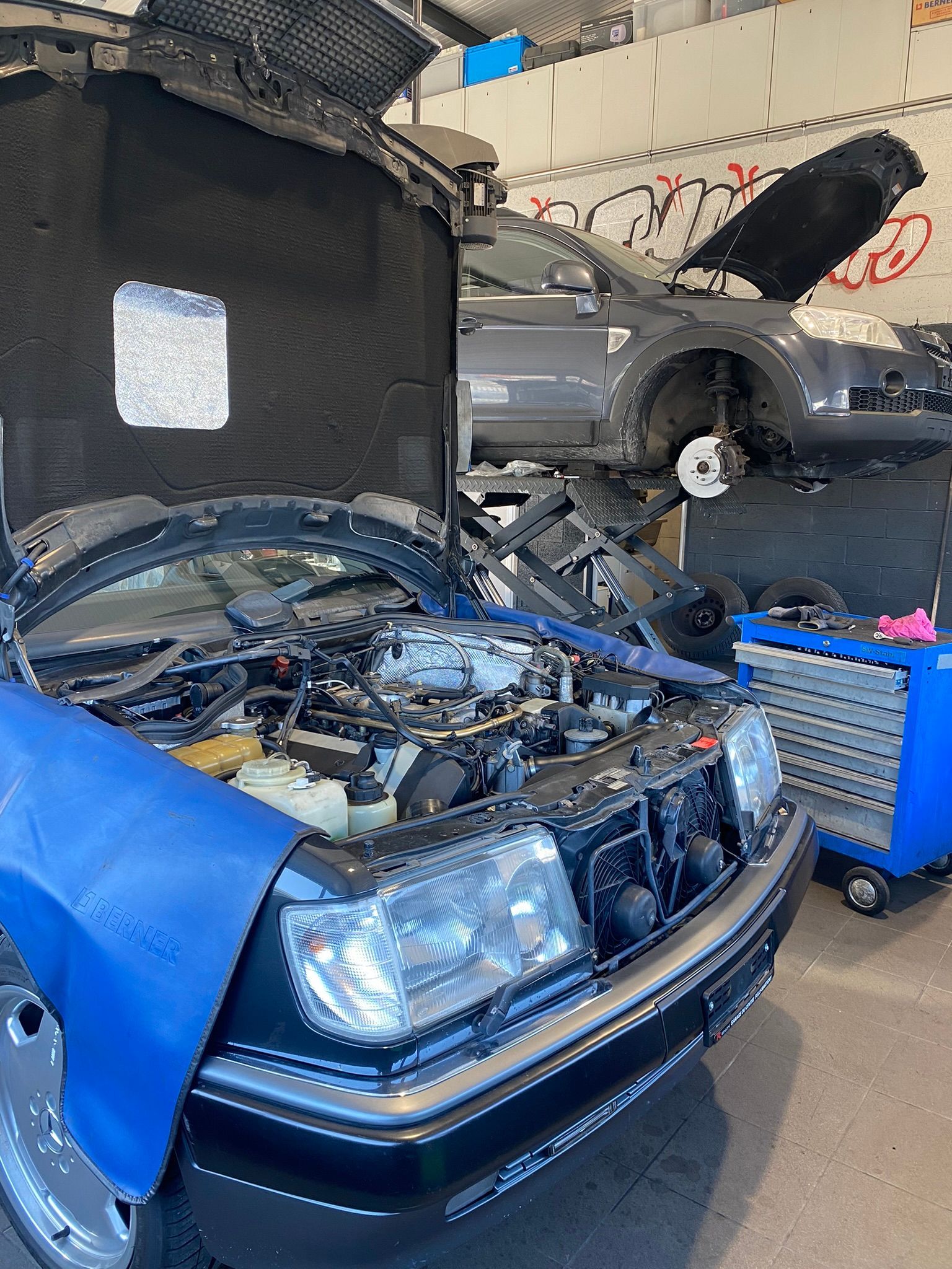 Une voiture est en travaux dans un garage avec le capot ouvert.