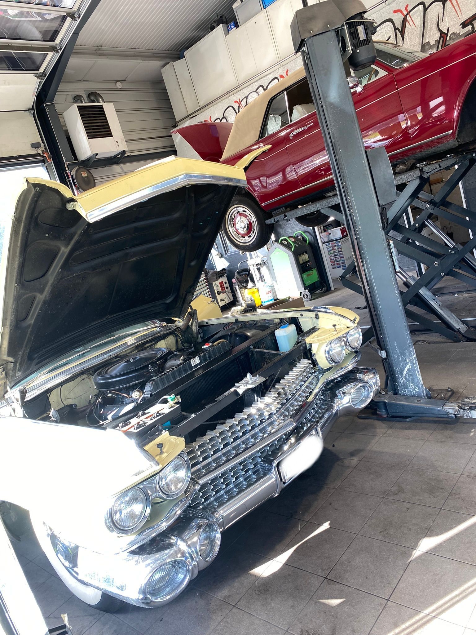Une voiture avec le capot ouvert est sur un ascenseur dans un garage.