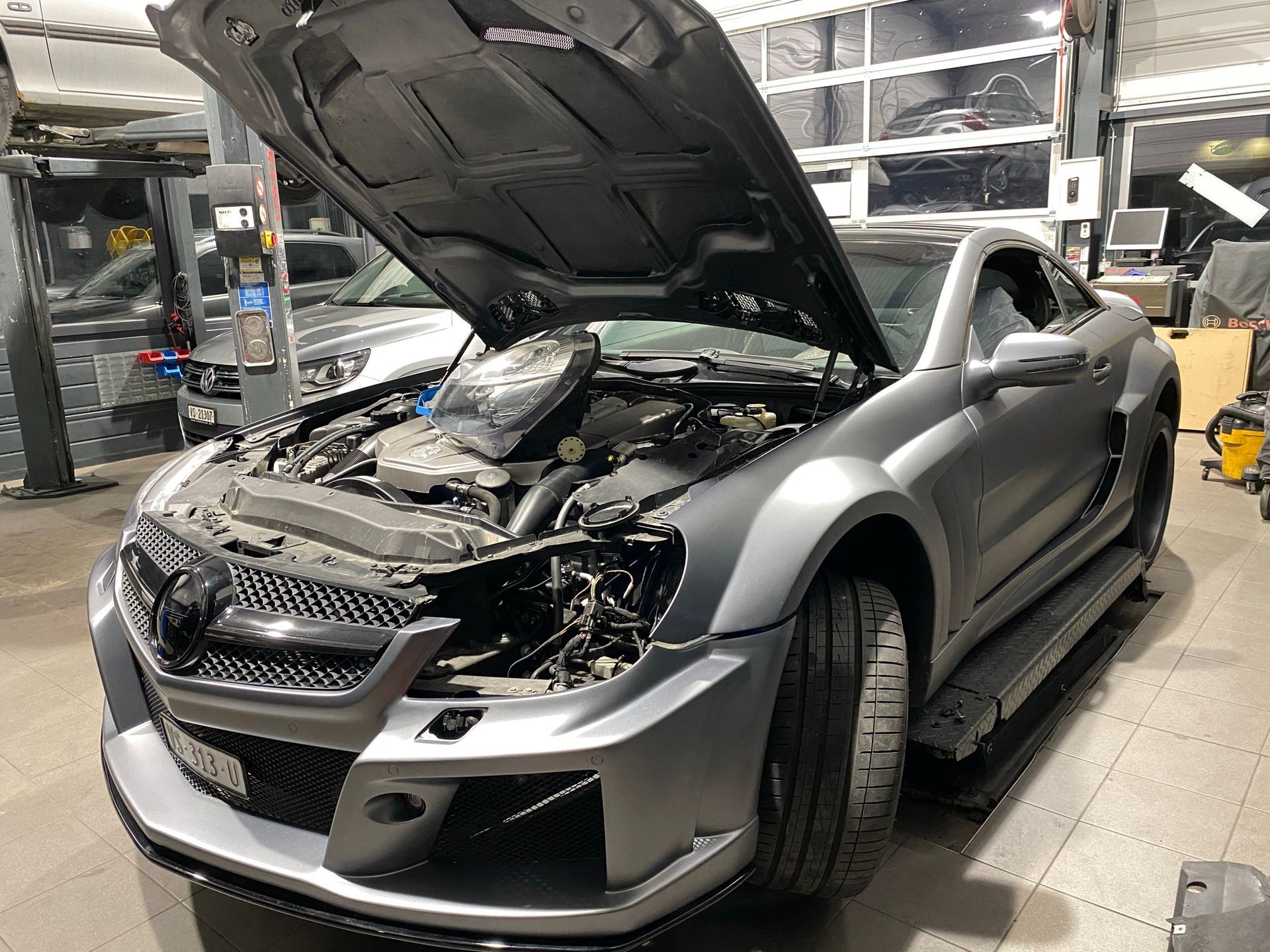 Une voiture de sport argentée avec le capot relevé dans un garage.