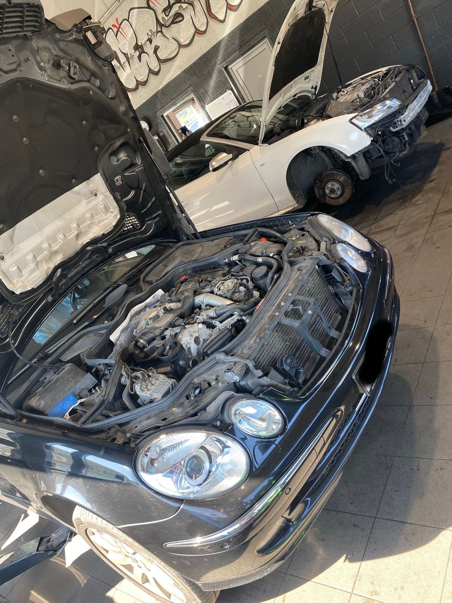 Une voiture noire avec le capot relevé est assise dans un garage.