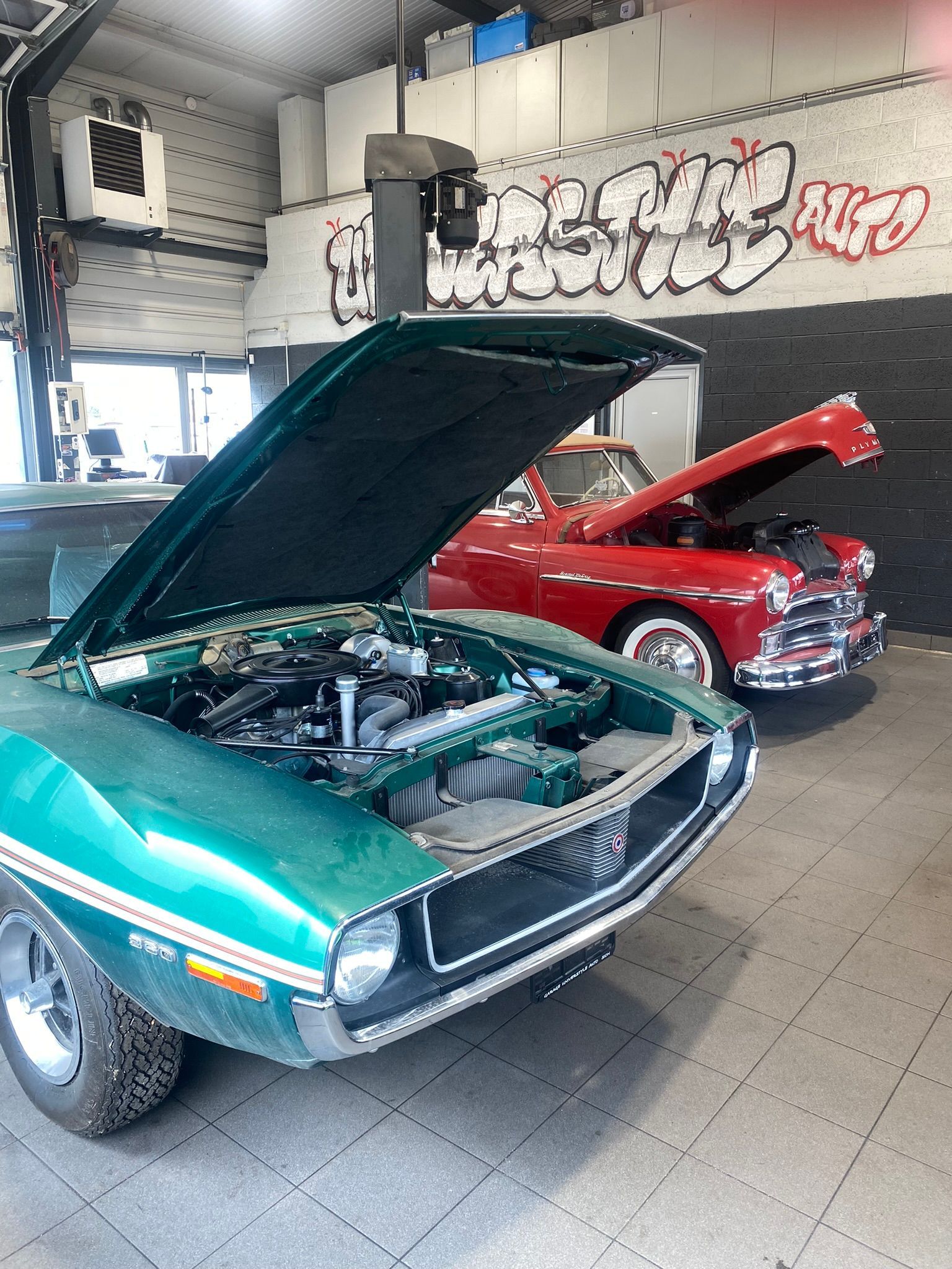 Une voiture verte avec le capot relevé est garée à côté d'une voiture rouge