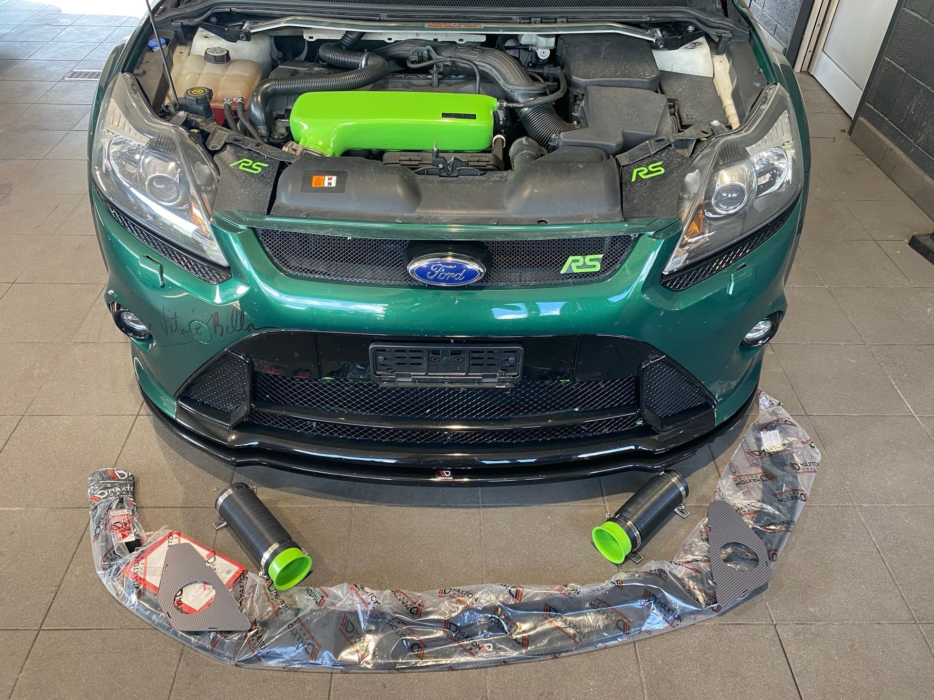Une Ford Focus verte avec le capot relevé est posée sur un sol carrelé.