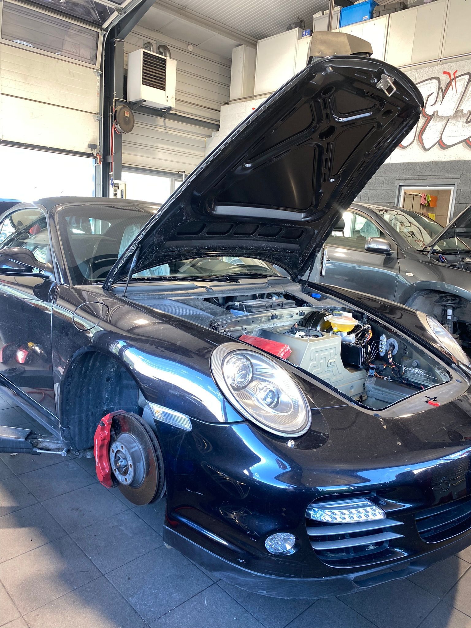 Une voiture noire avec le capot relevé est garée dans un garage.