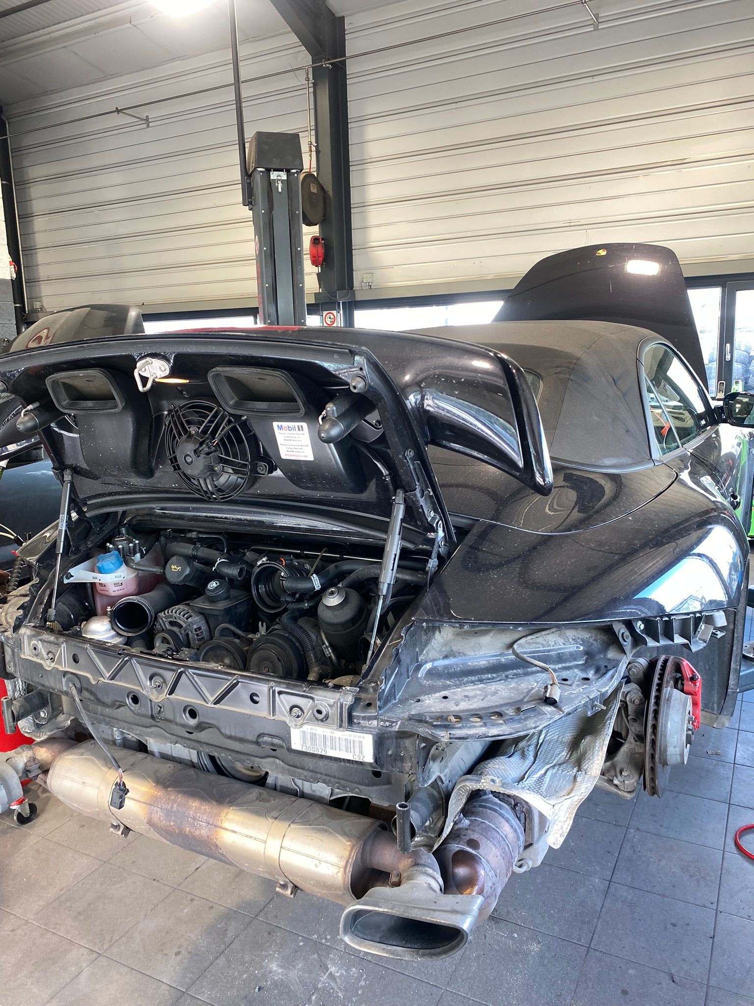 Une voiture noire avec le capot relevé est assise dans un garage.