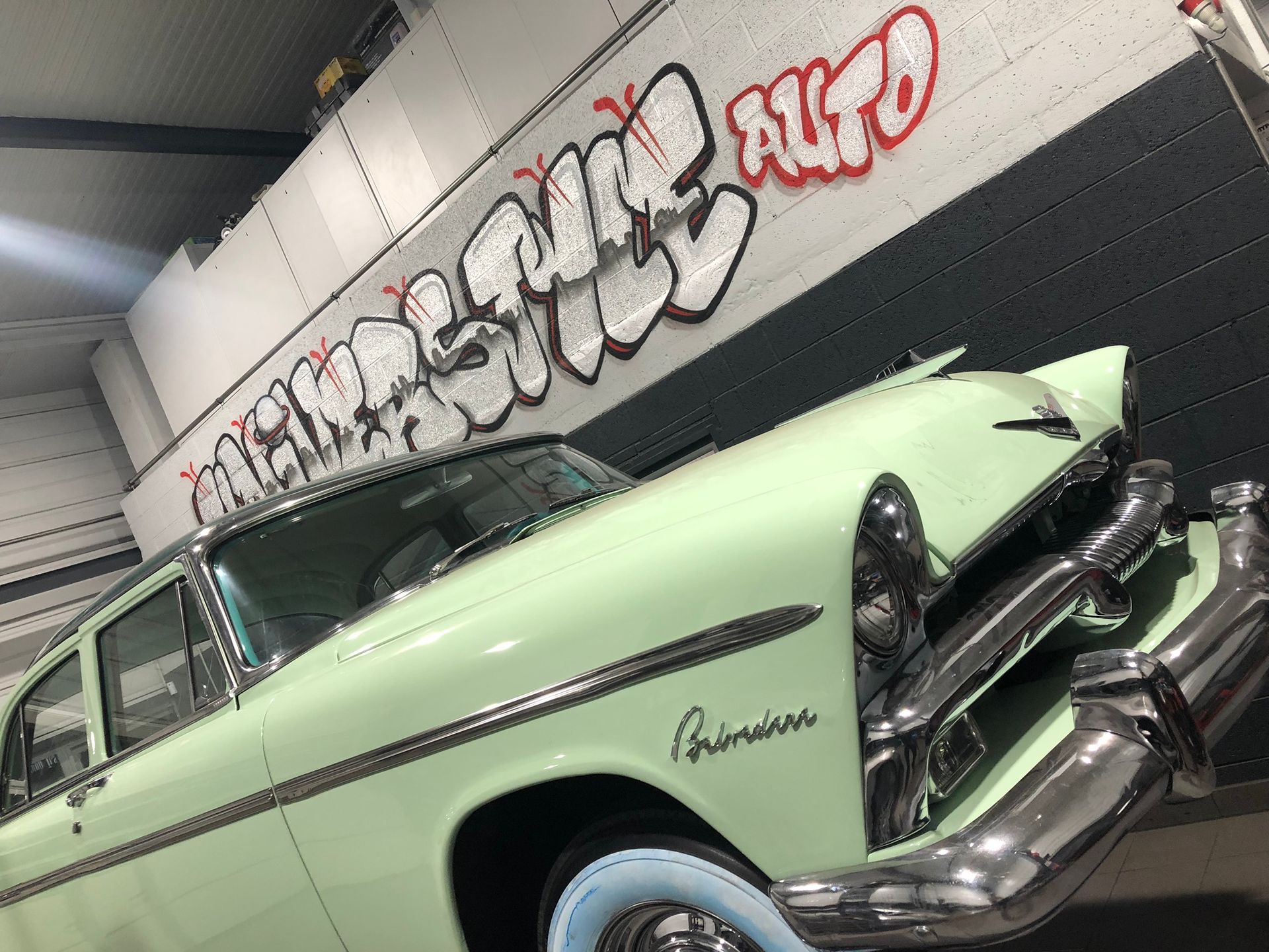 Une voiture verte est garée devant un mur avec des graffitis dessus.