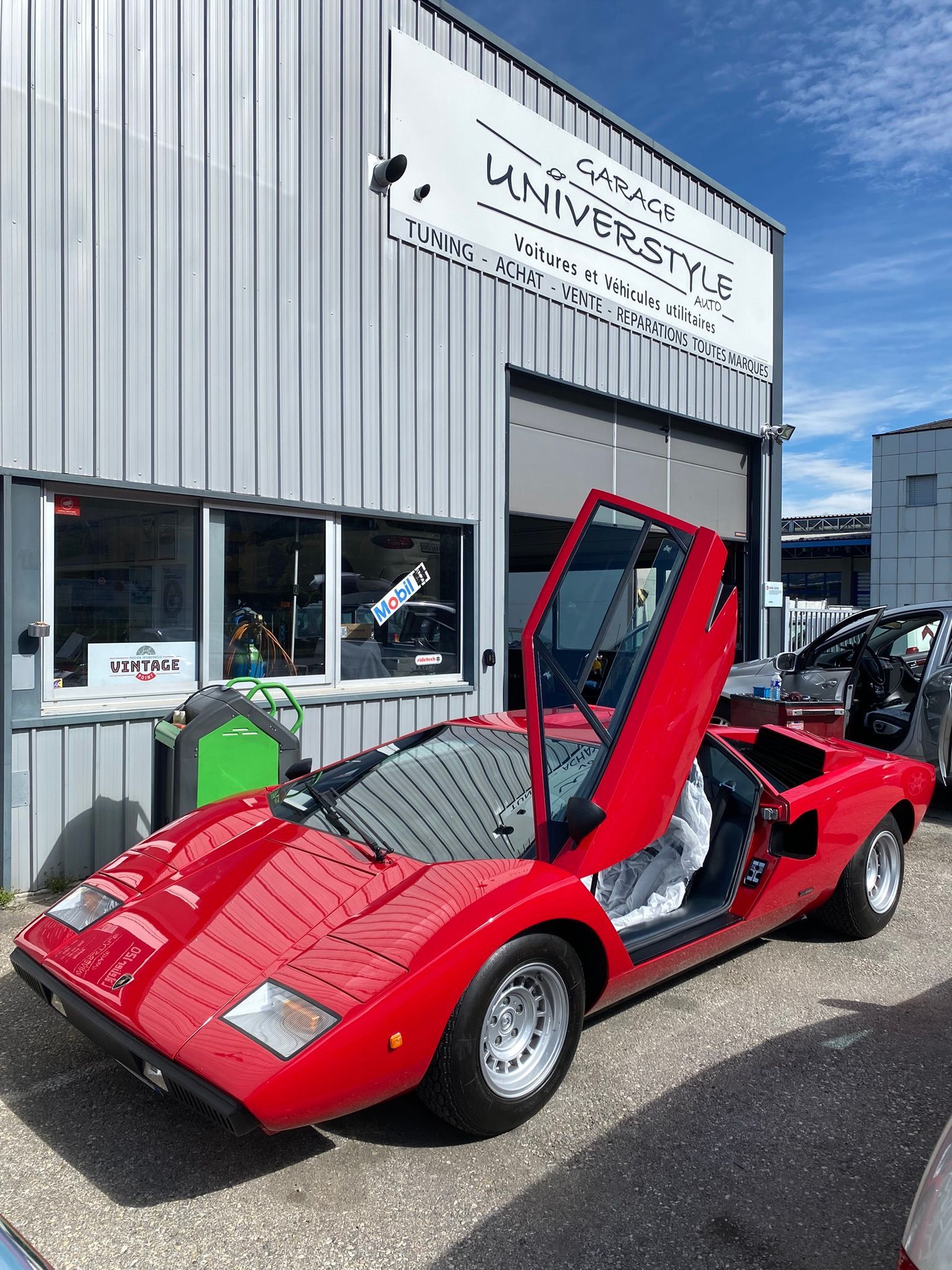 Une voiture de sport rouge est garée devant un immeuble avec ses portes ouvertes.