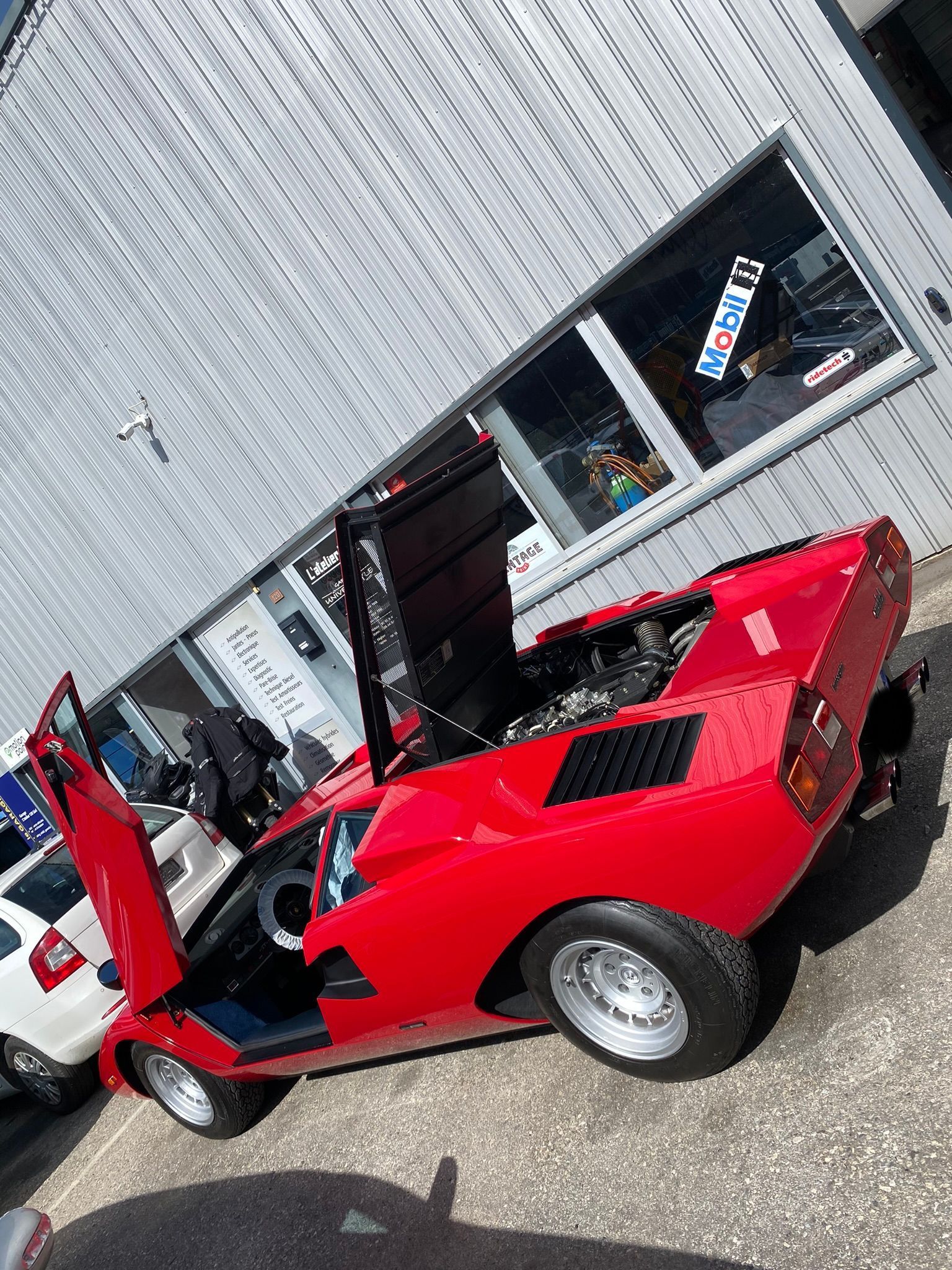 Une voiture de sport rouge est garée devant un immeuble avec ses portes ouvertes.