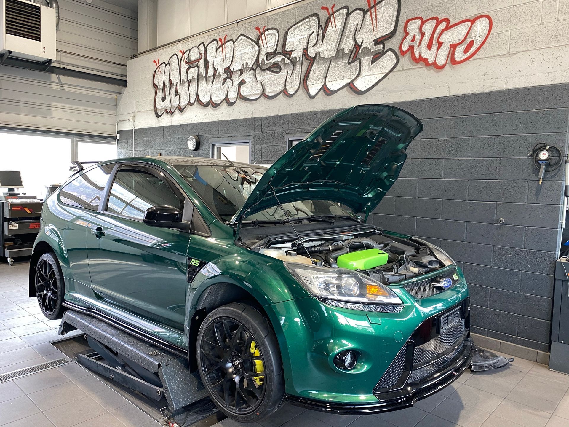 Une voiture verte avec le capot ouvert est garée dans un garage.