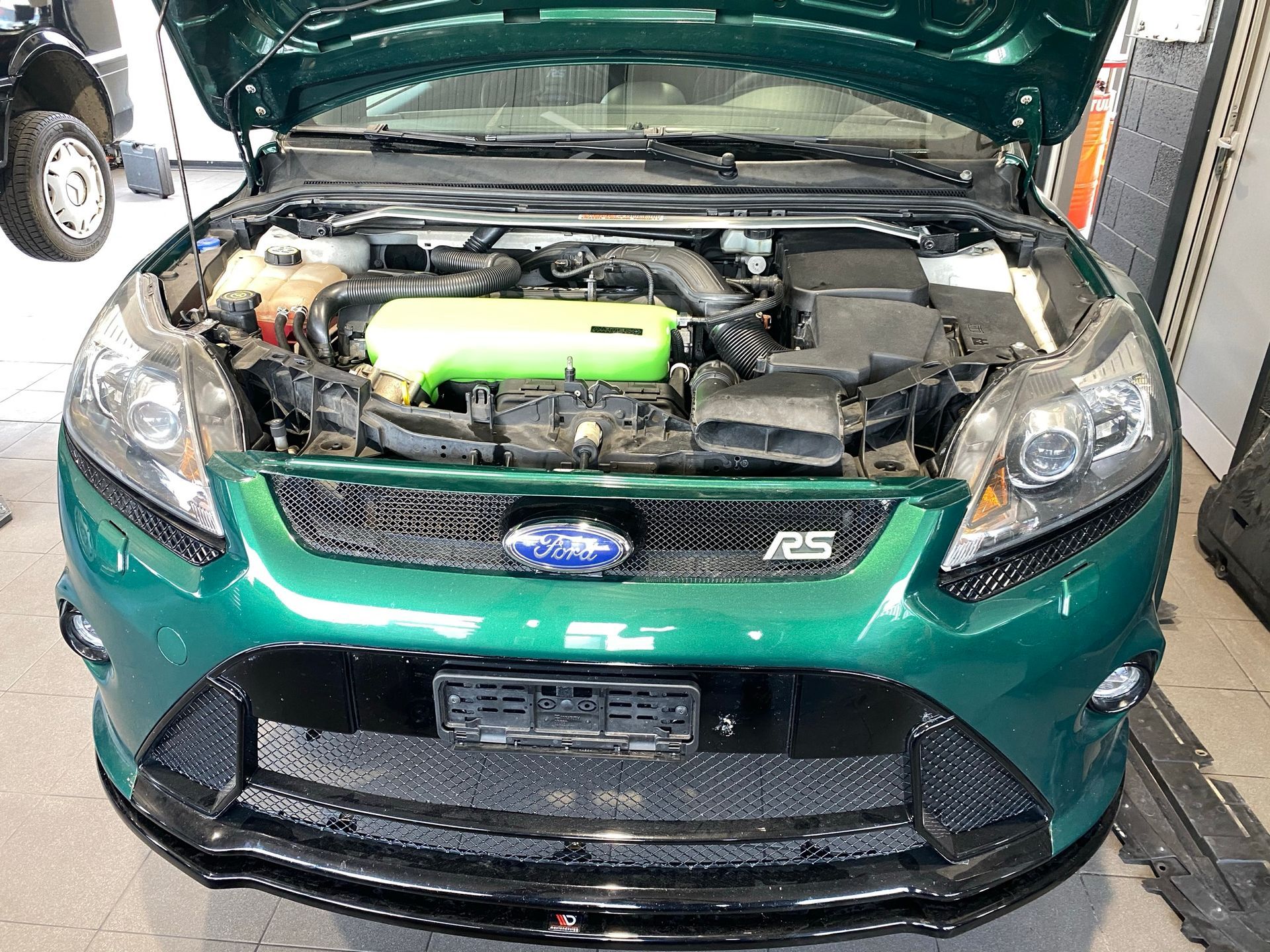 Une Ford Focus verte avec le capot ouvert se trouve dans un garage.