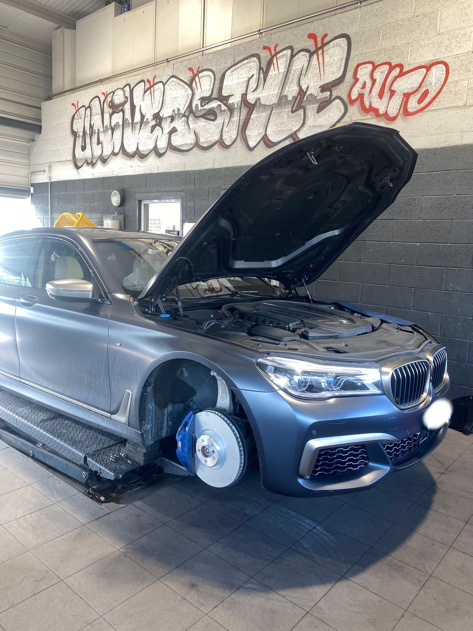 Une BMW est assise sur un ascenseur avec son capot ouvert dans un garage.