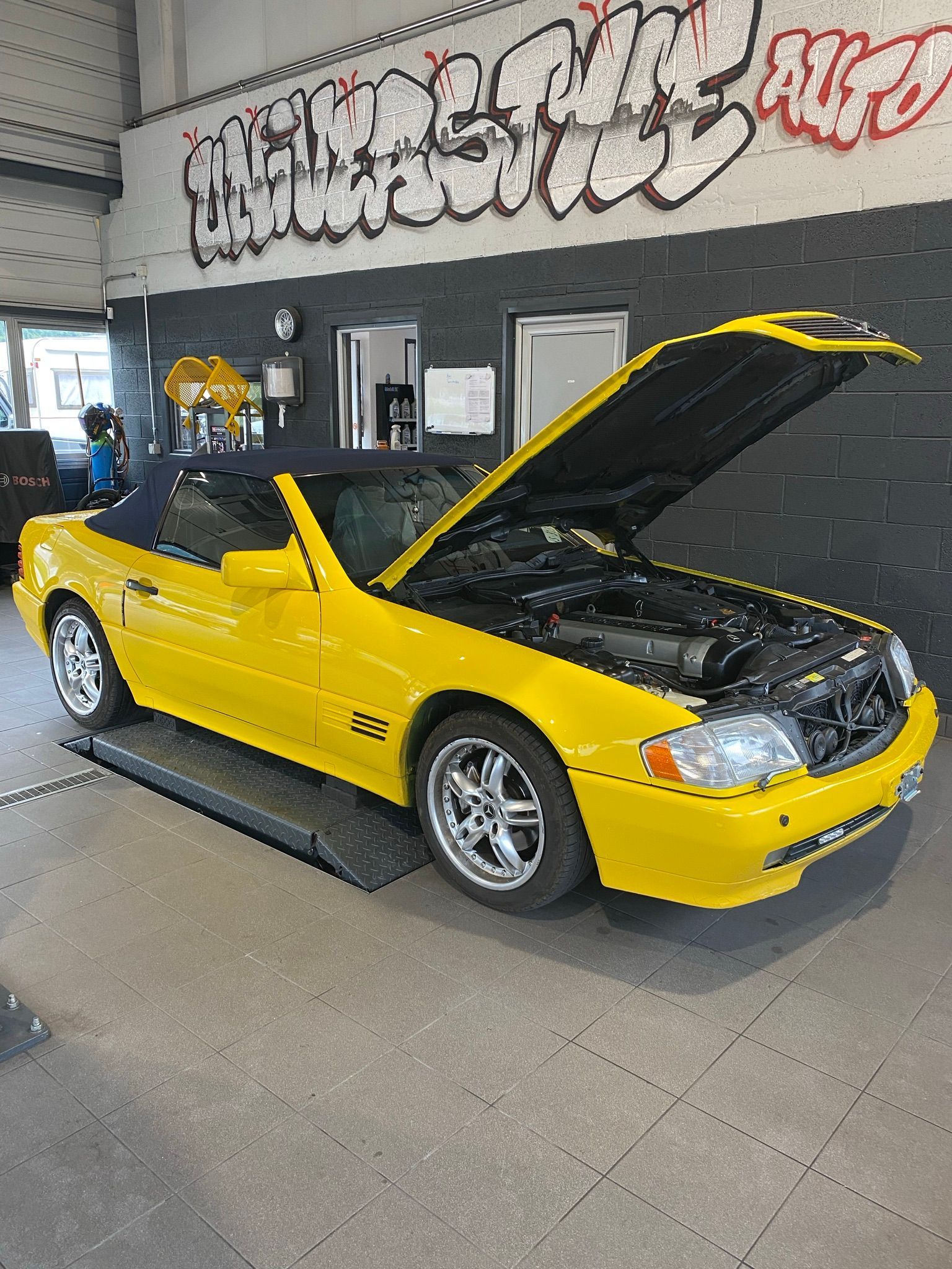 Une voiture décapotable jaune avec le capot relevé est garée dans un garage.