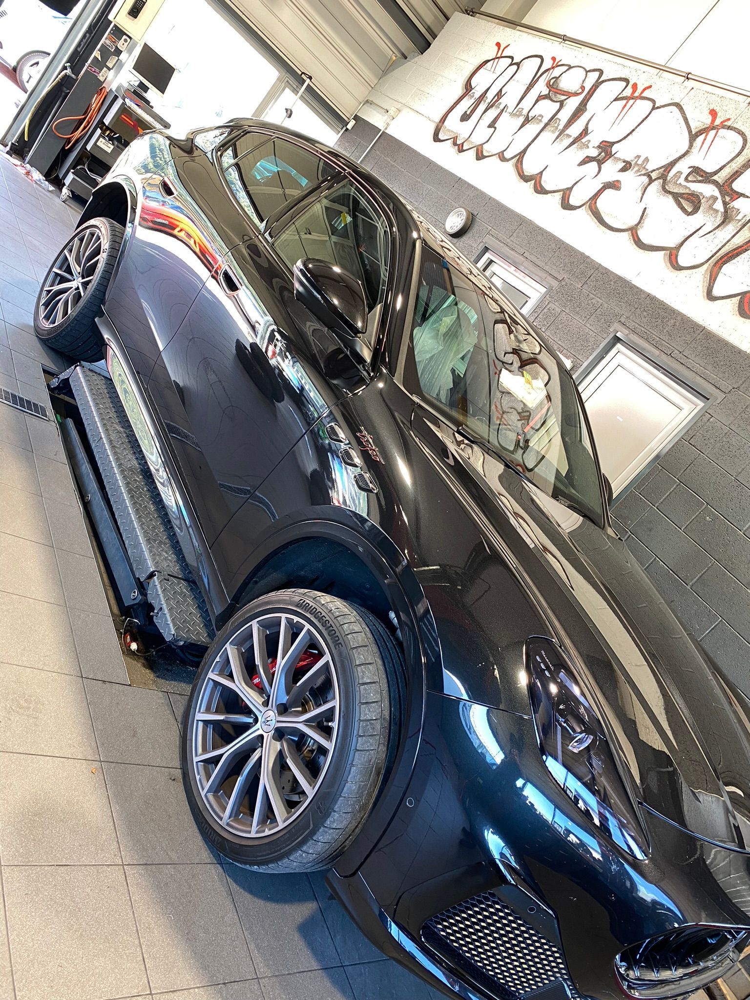 Une voiture noire est garée dans un garage avec des graffitis sur le mur.