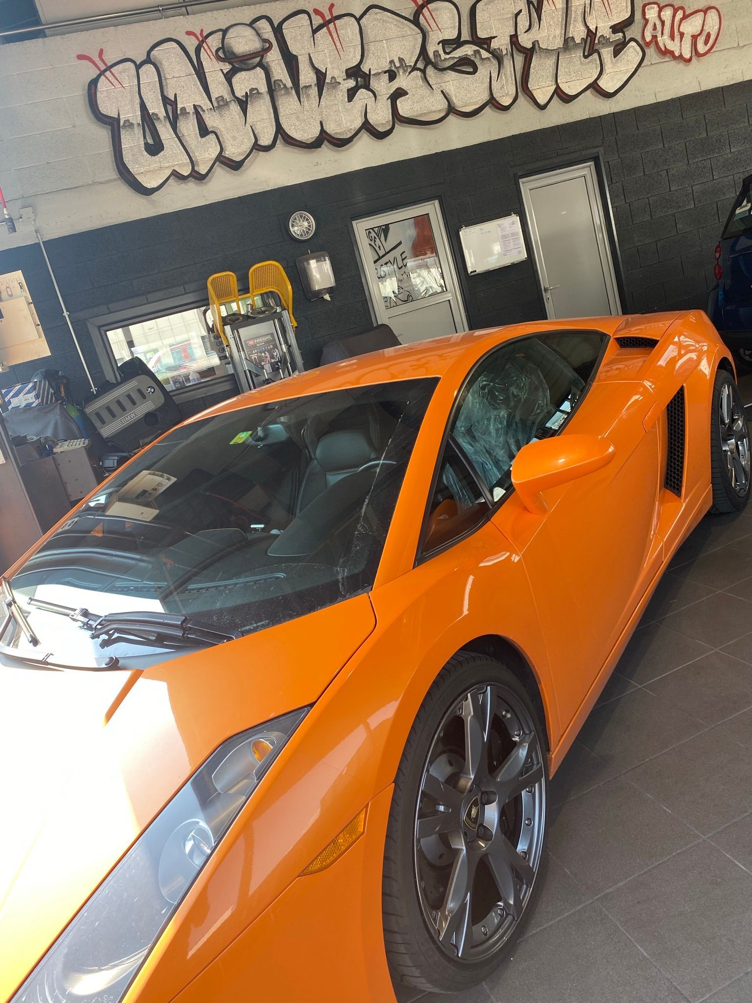 Une voiture de sport orange est garée devant un bâtiment avec des graffitis dessus